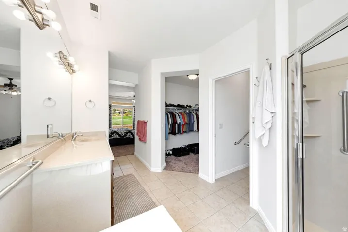 Ensuite bathroom with vanity, a walk in closet, light tile patterned floors, and a shower stall