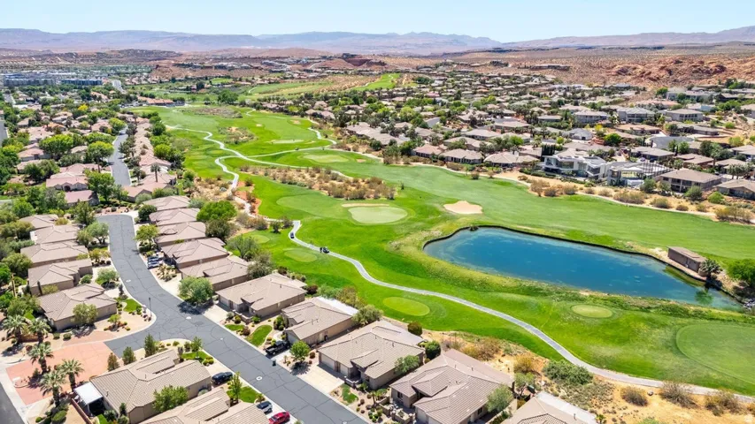 Aerial view of property and surrounding area featuring nearby suburban area, a water and mountain view, and a golf course