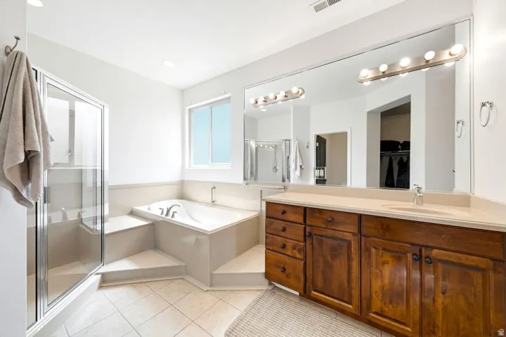 Bathroom with a shower stall, vanity, light tile patterned flooring, a bath, and a walk in closet