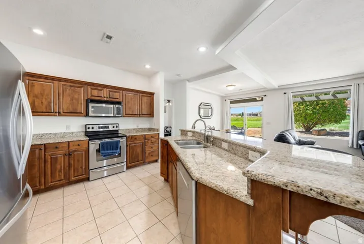 Kitchen with stainless steel appliances, light stone counters, wood finish cabinets, recessed lighting, and a textured ceiling