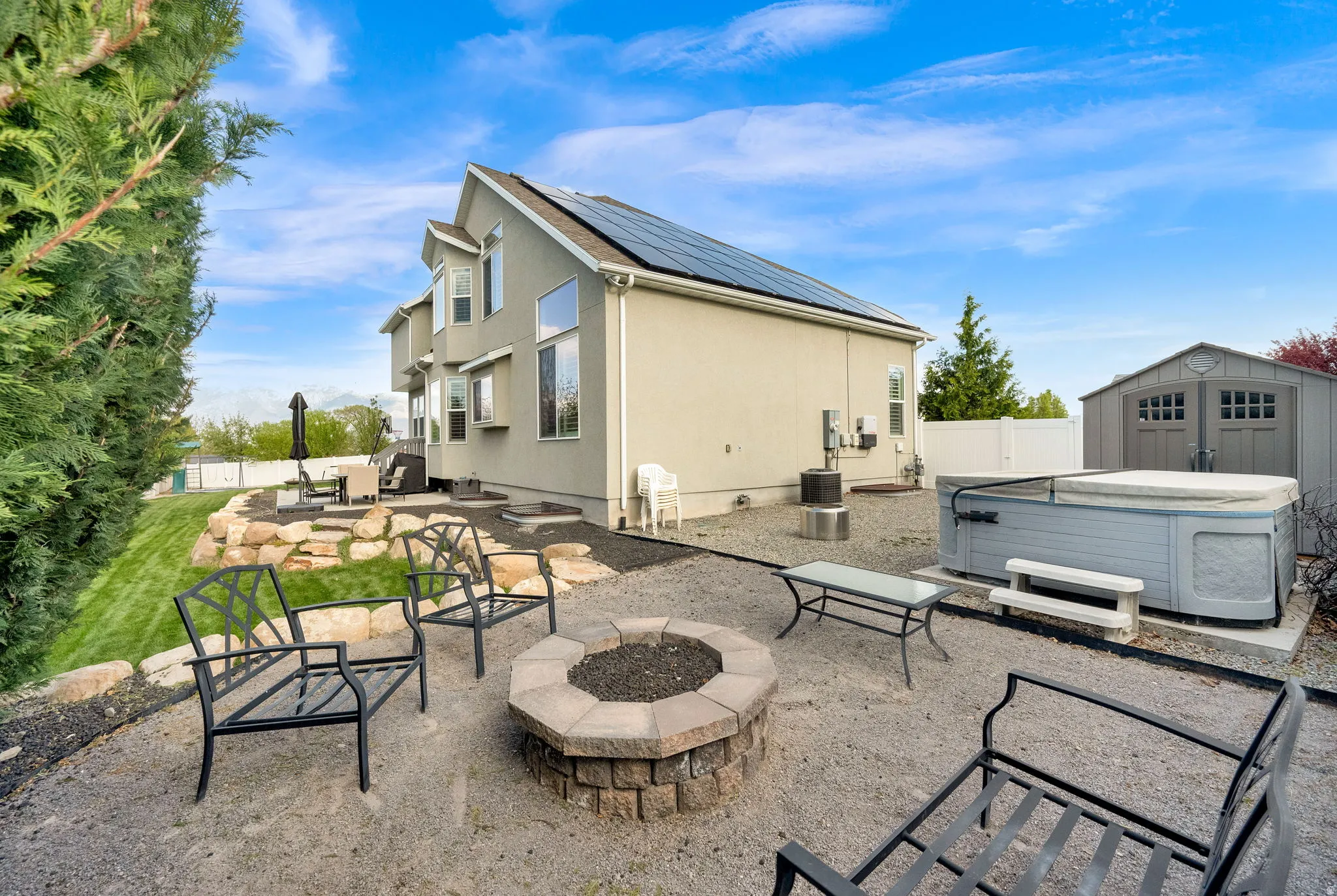 Fenced backyard with a patio area, a storage unit, an outdoor fire pit, and a hot tub