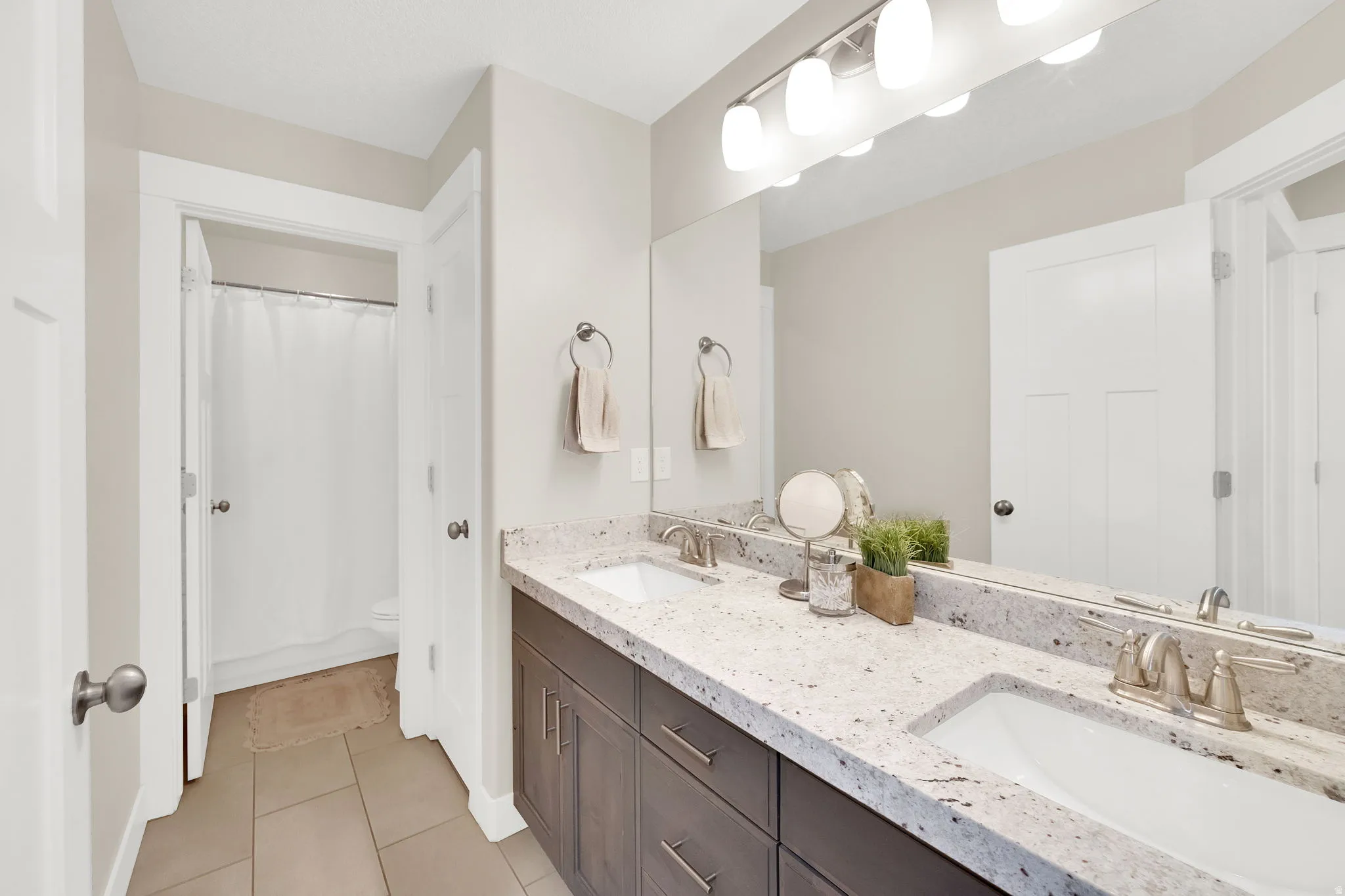 Full bathroom featuring double vanity, light tile patterned flooring, and curtained shower