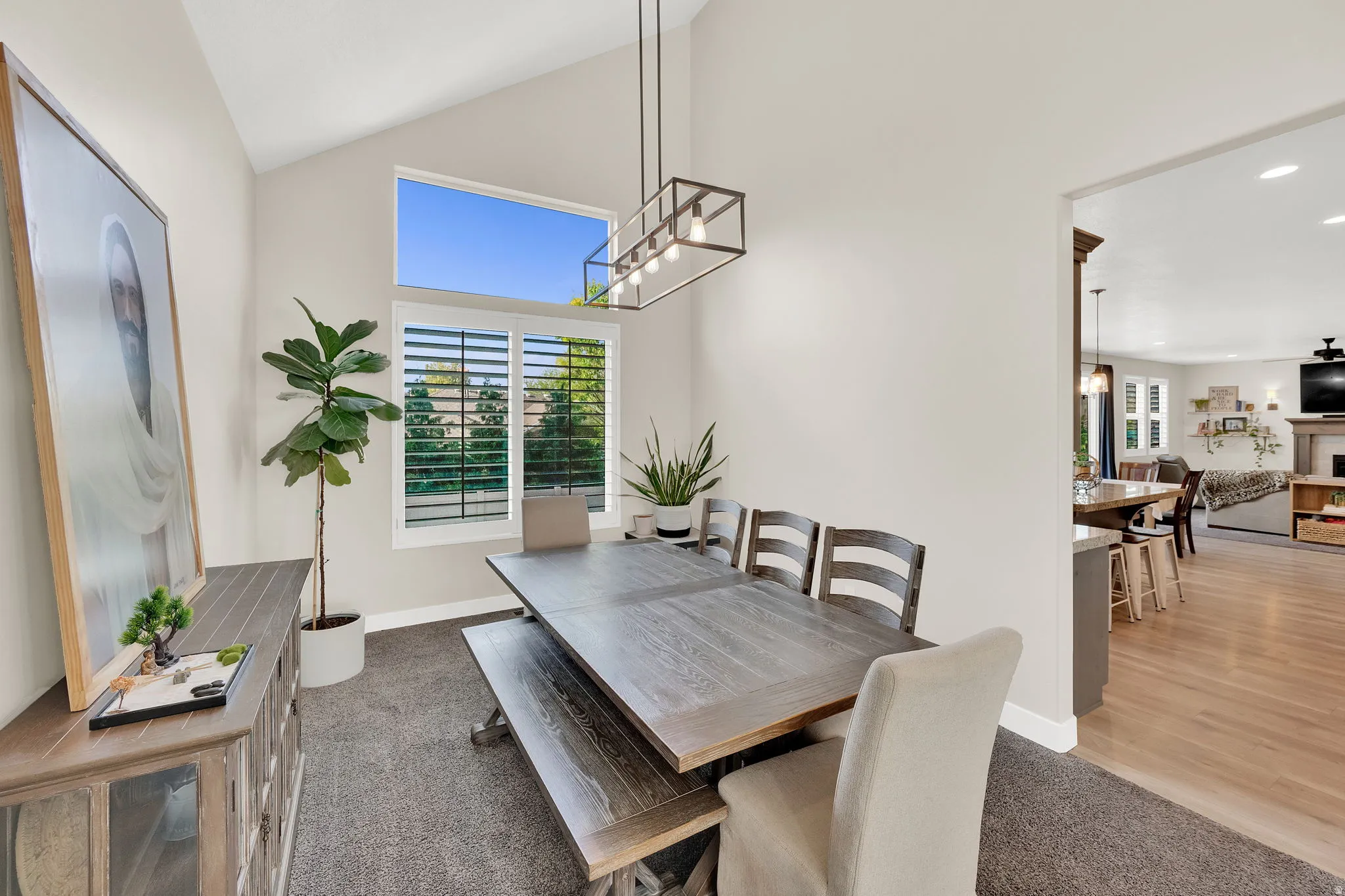 Dining area with plenty of natural light, light colored carpet, hanging lights, vaulted ceiling, and a fireplace