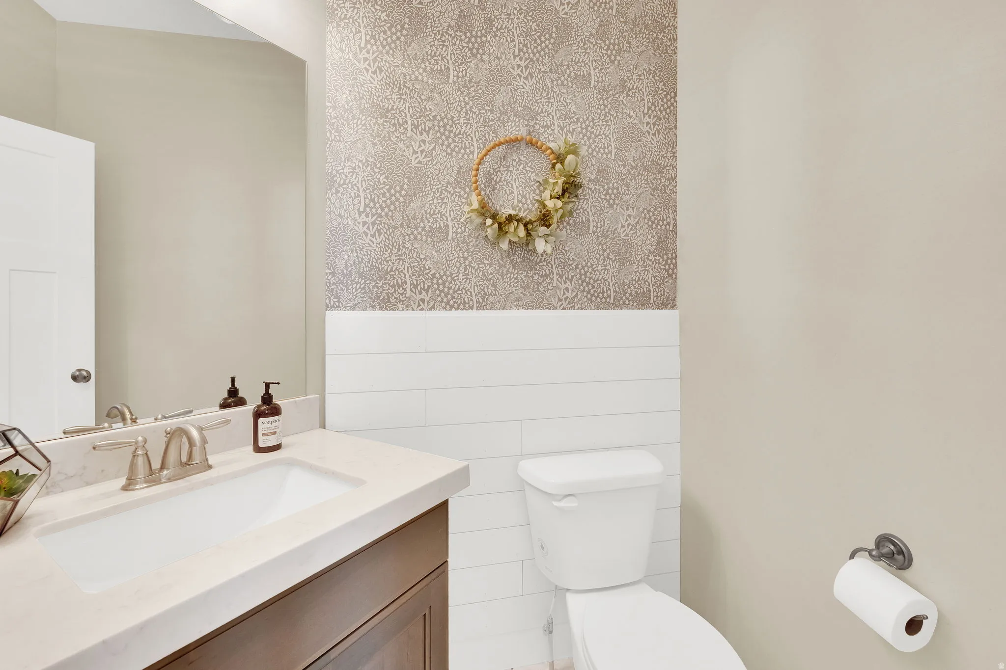 Half bathroom with vanity, wallpapered walls, and wainscoting