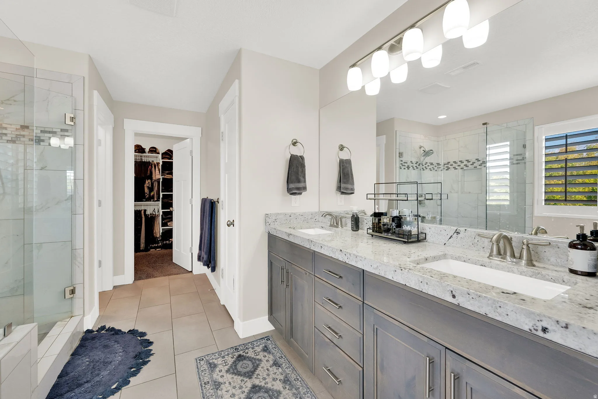 Full bathroom with a stall shower, double vanity, a spacious closet, and light tile patterned floors