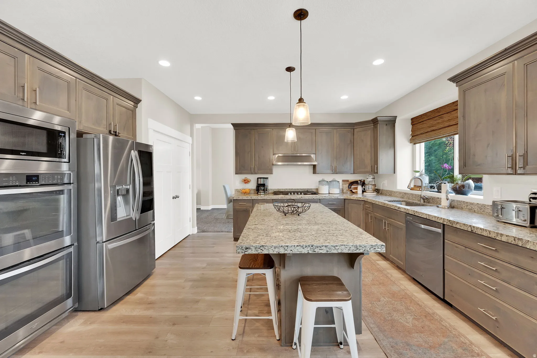 Kitchen featuring stainless steel appliances, a breakfast bar, a kitchen island, hanging light fixtures, and light wood-type flooring