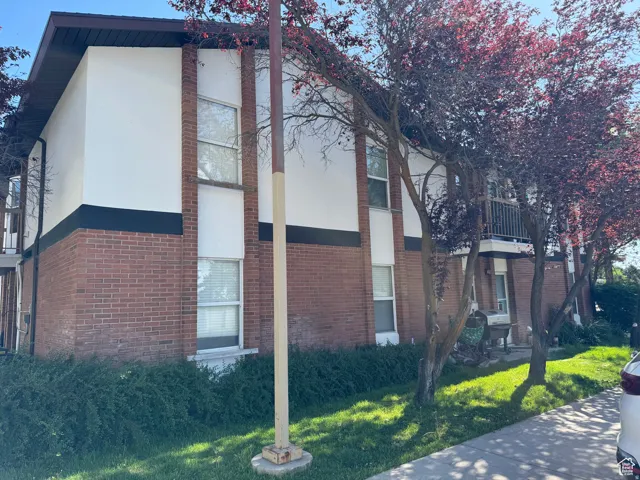 View of property exterior with stucco siding, a balcony, brick siding, and a yard