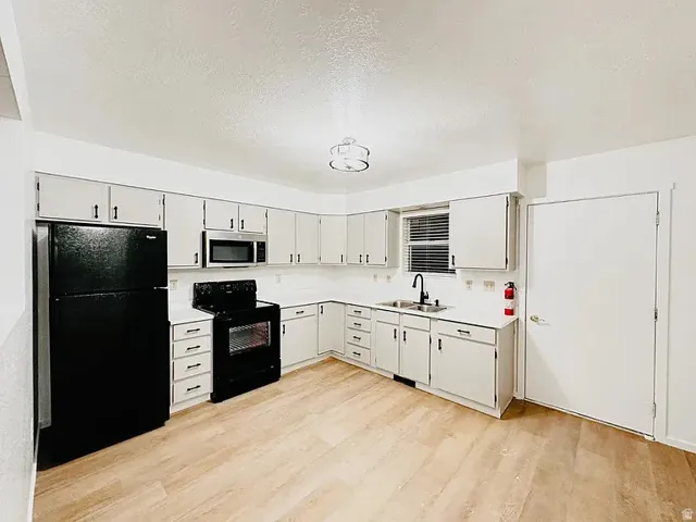 Kitchen with light countertops, black appliances, a textured ceiling, and light wood-type flooring