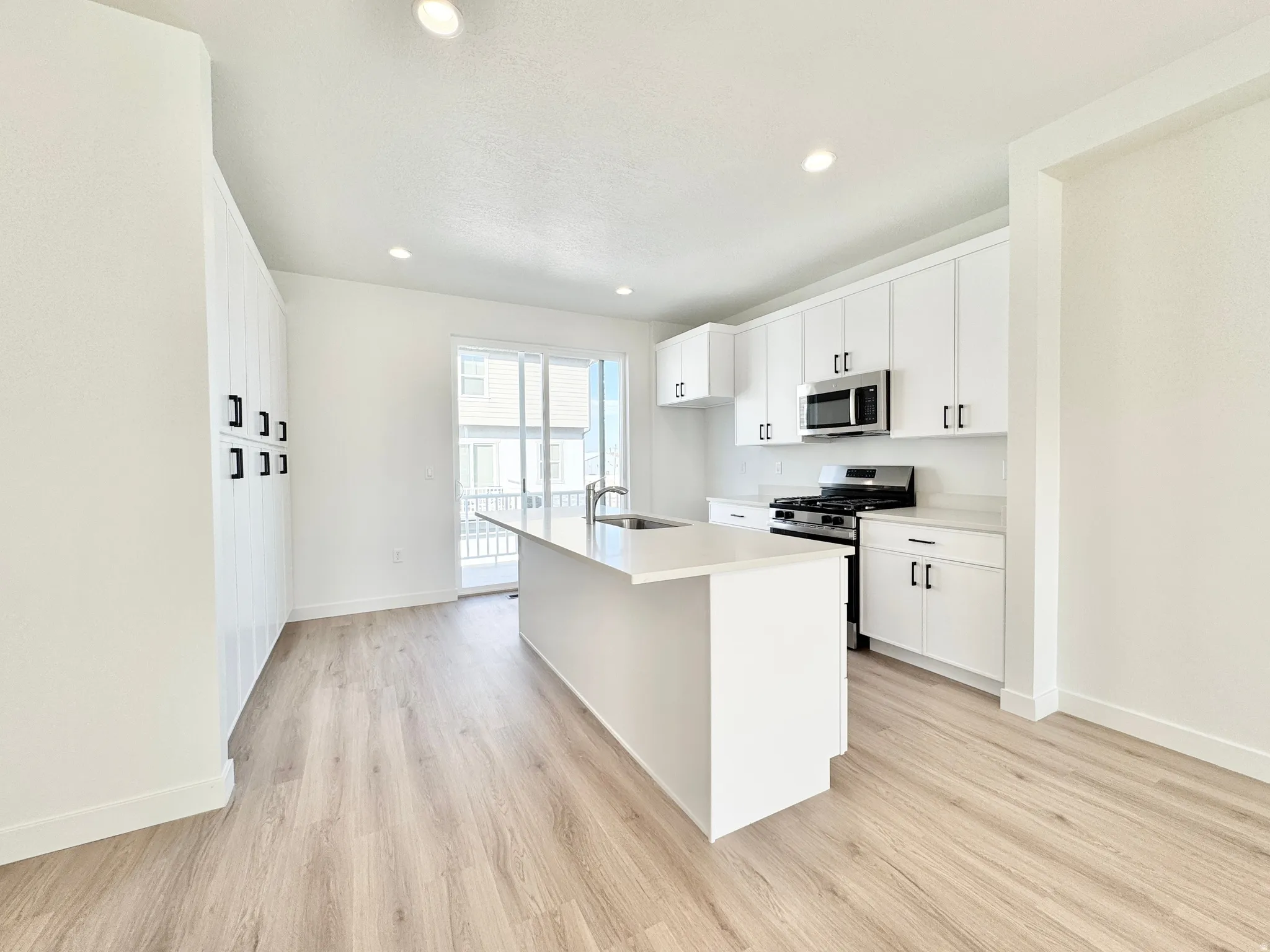 Kitchen featuring stainless steel appliances, white cabinets, light wood-style floors, an island with sink, and recessed lighting