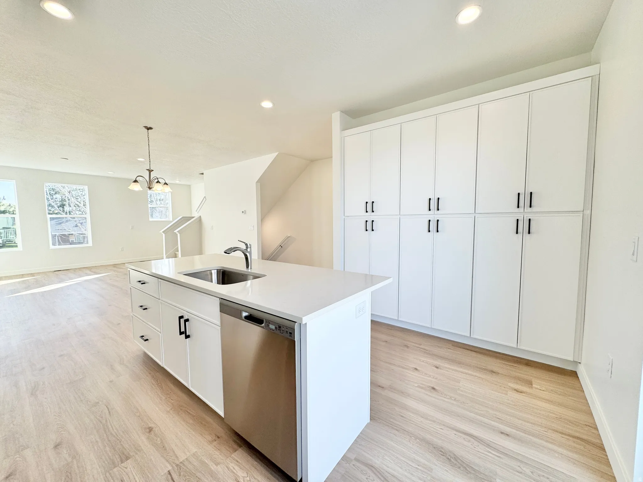 Kitchen featuring dishwasher, white cabinetry, light wood-style floors, a kitchen island with sink, and open floor plan