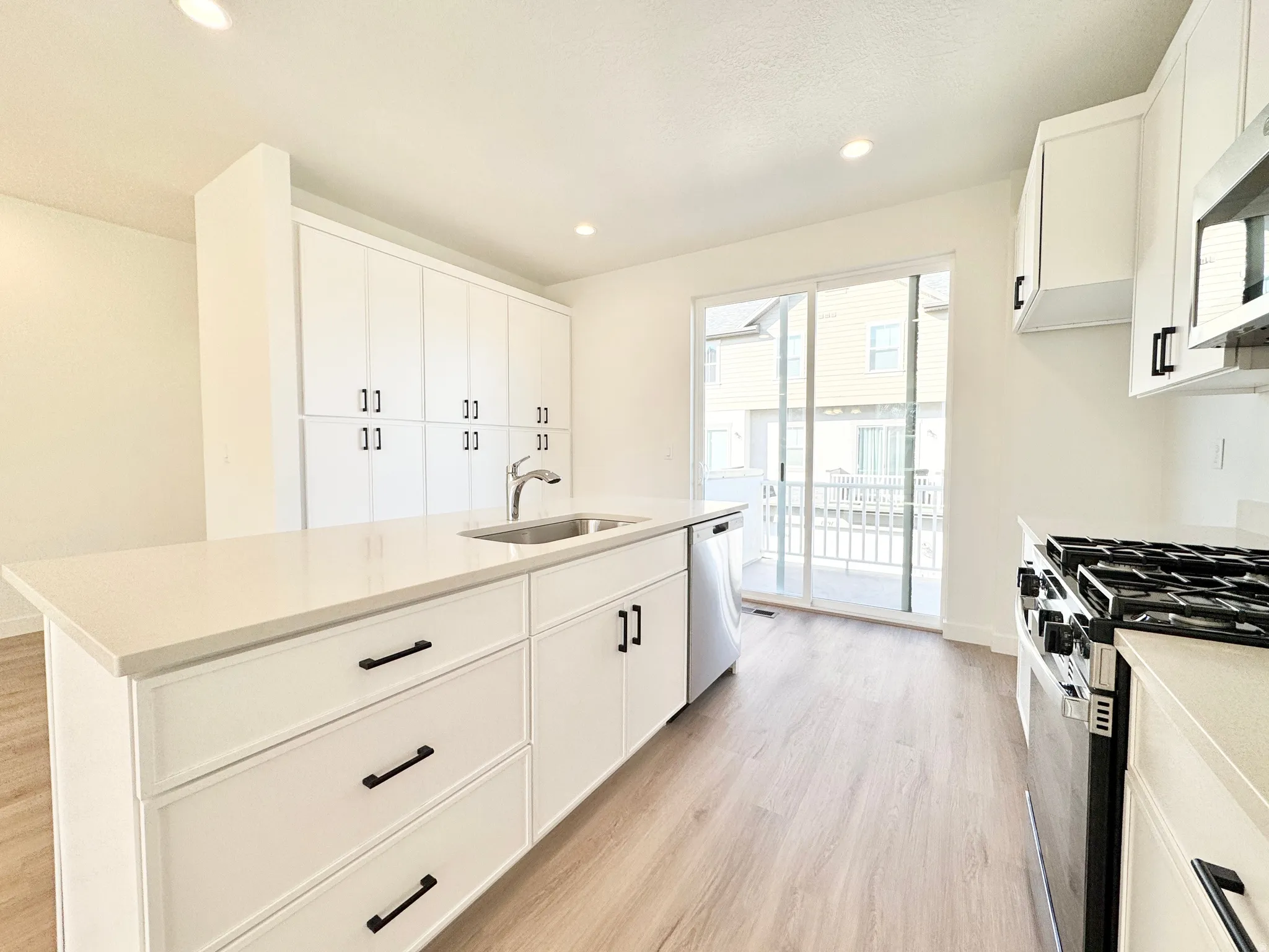 Kitchen with stainless steel appliances, a kitchen island with sink, light wood-style flooring, white cabinets, and recessed lighting