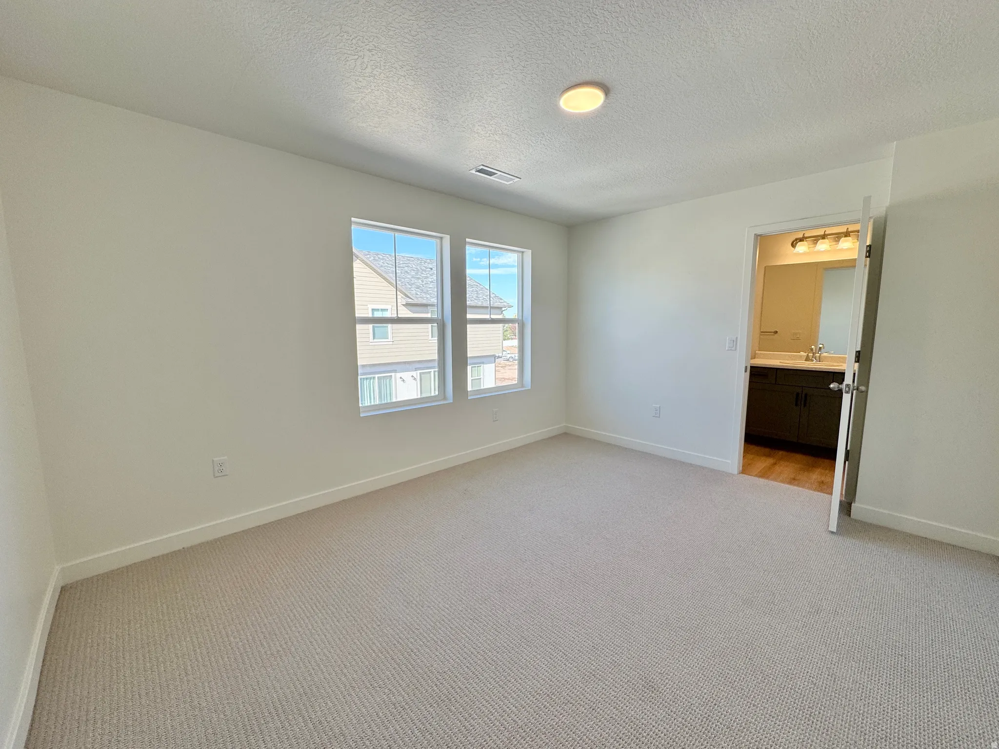 Unfurnished bedroom featuring light colored carpet, a textured ceiling, and ensuite bathroom