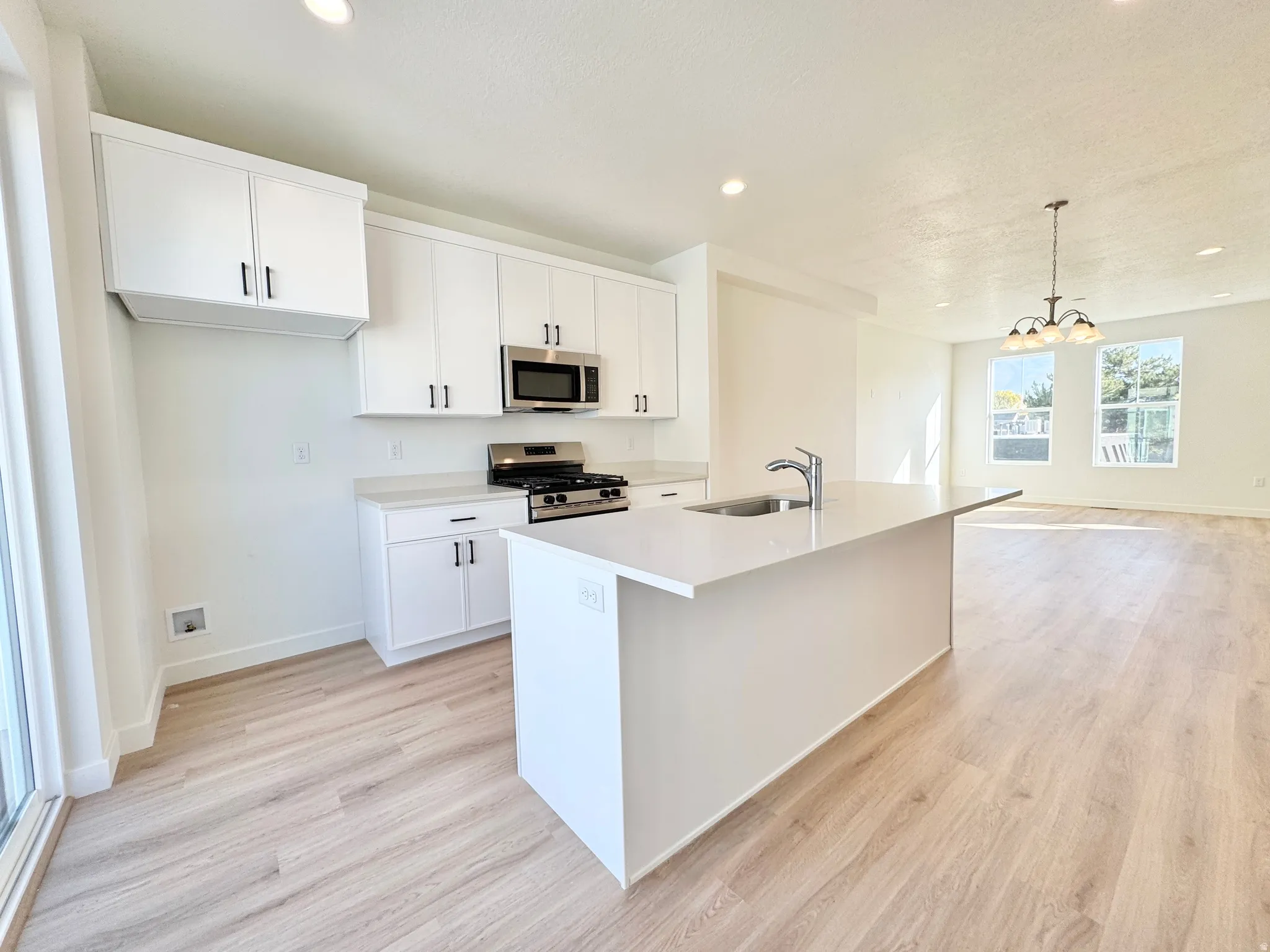 Kitchen featuring white cabinetry, stainless steel appliances, light wood-style floors, and a center island with sink