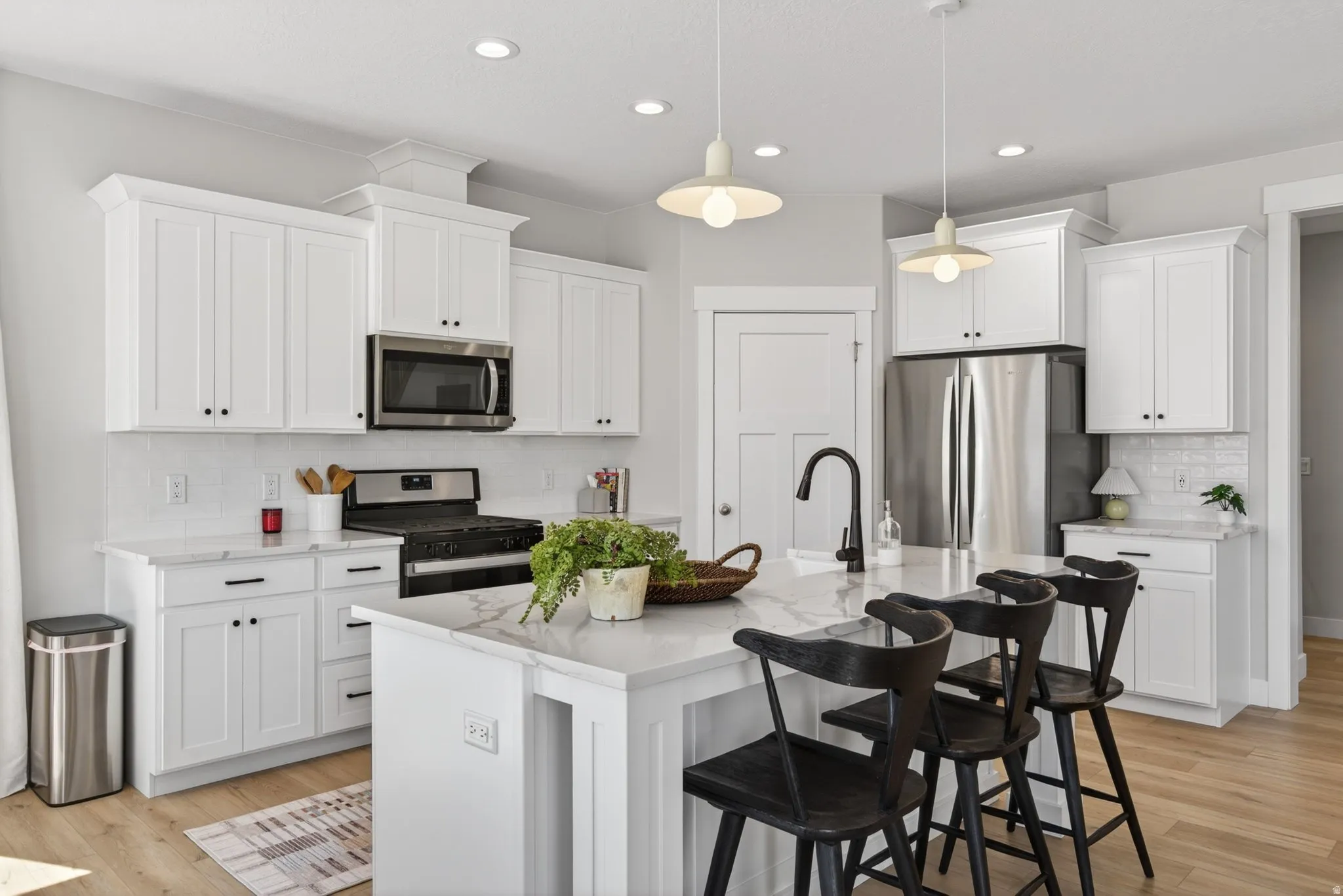 Kitchen featuring stainless steel appliances, decorative backsplash, white cabinets, and a breakfast bar