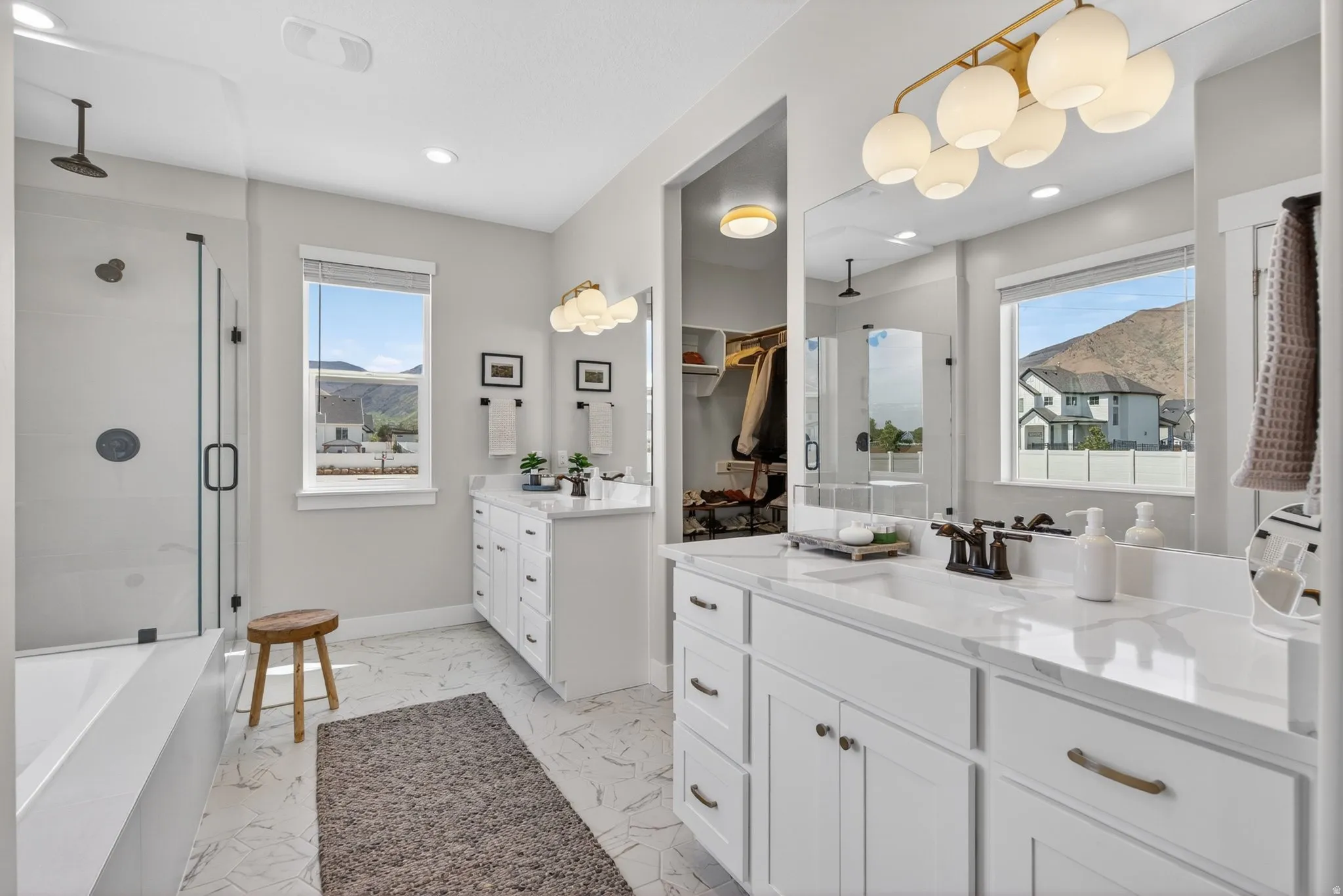 Full bathroom featuring a bath, a shower stall, two vanities, light marble finish flooring, and recessed lighting