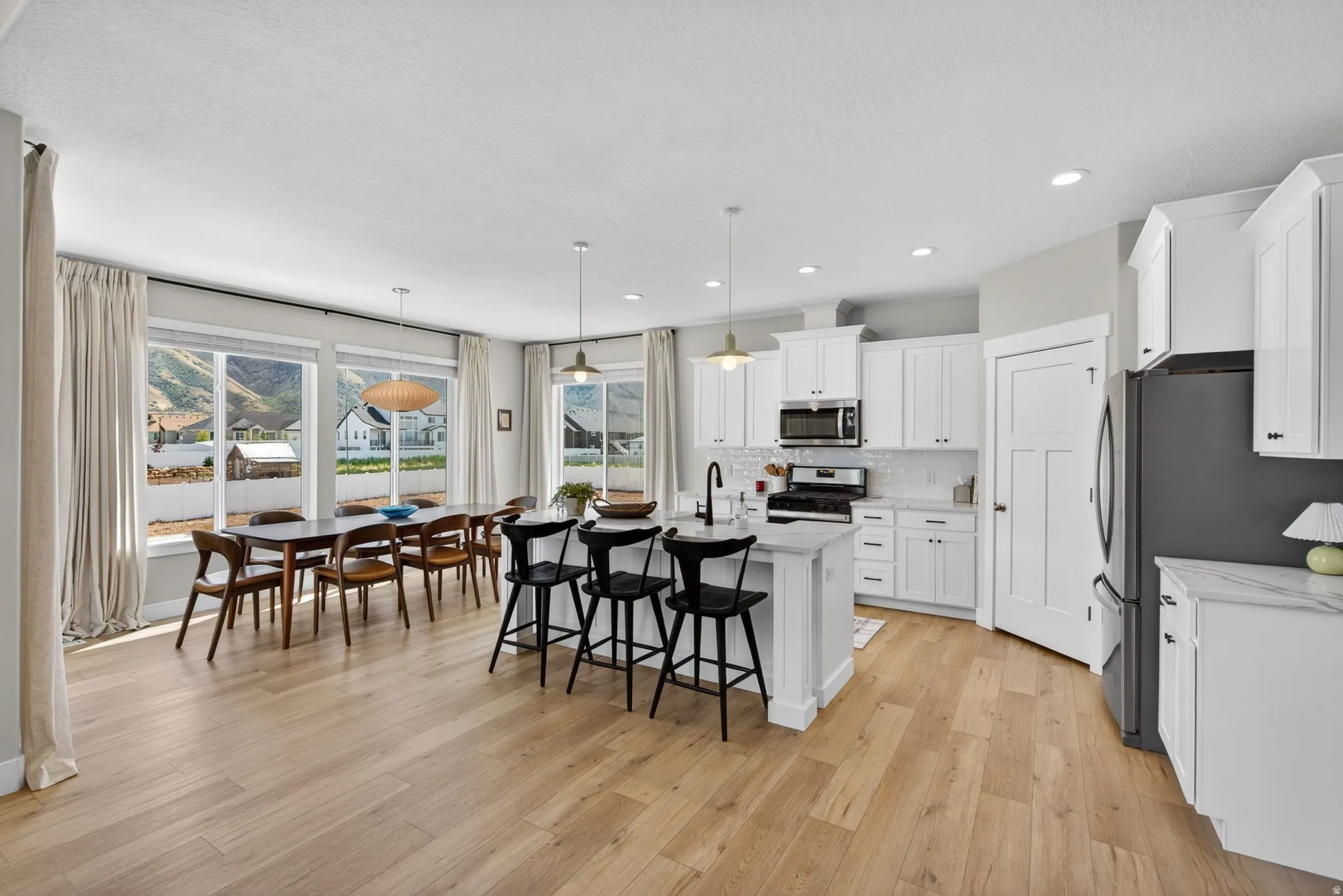 Kitchen with an island with sink, stainless steel appliances, white cabinets, a kitchen bar, and light wood-style flooring