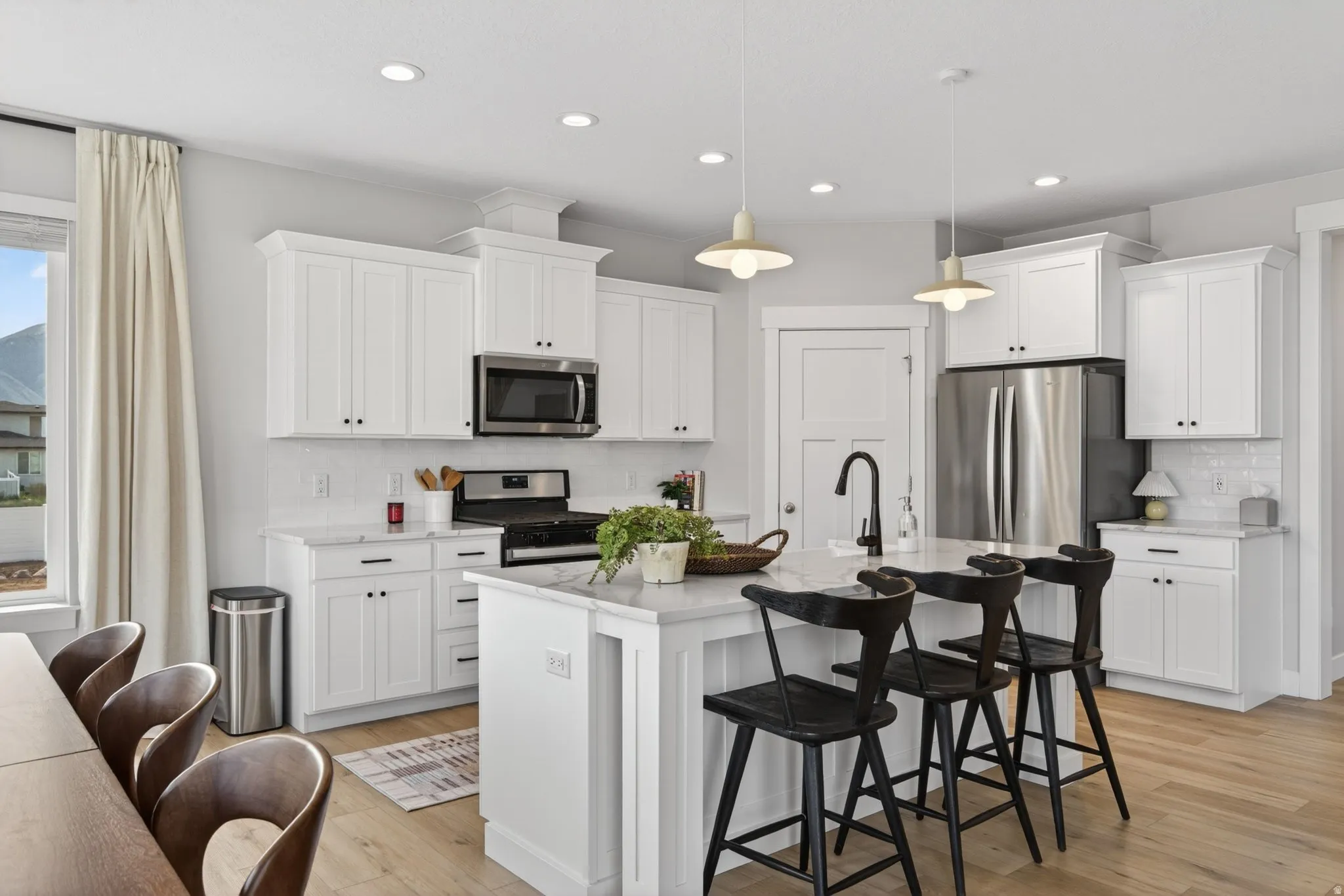 Kitchen with a breakfast bar area, decorative backsplash, stainless steel appliances, white cabinets, and a kitchen island with sink