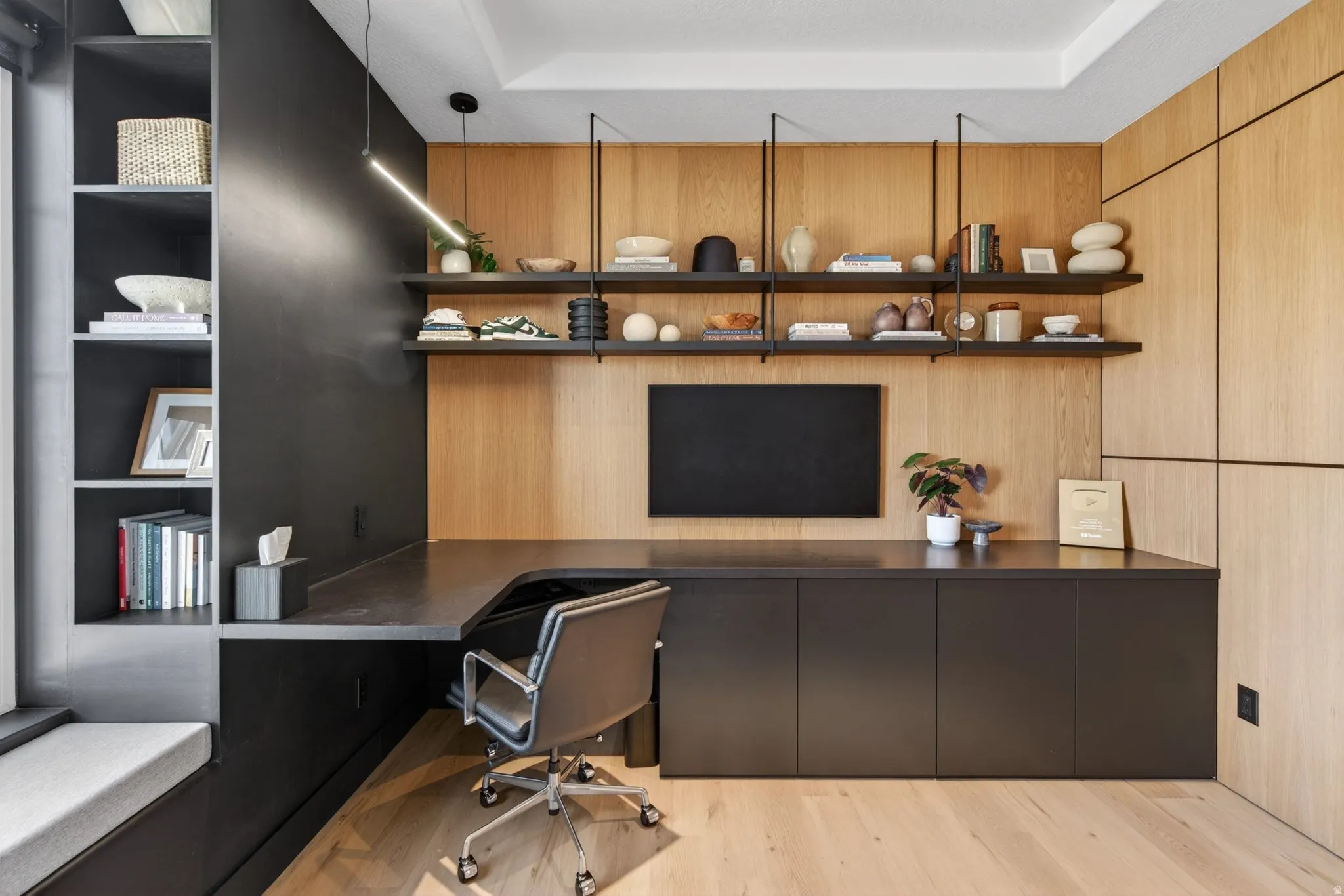Office space with built in desk, light wood-type flooring, and a tray ceiling