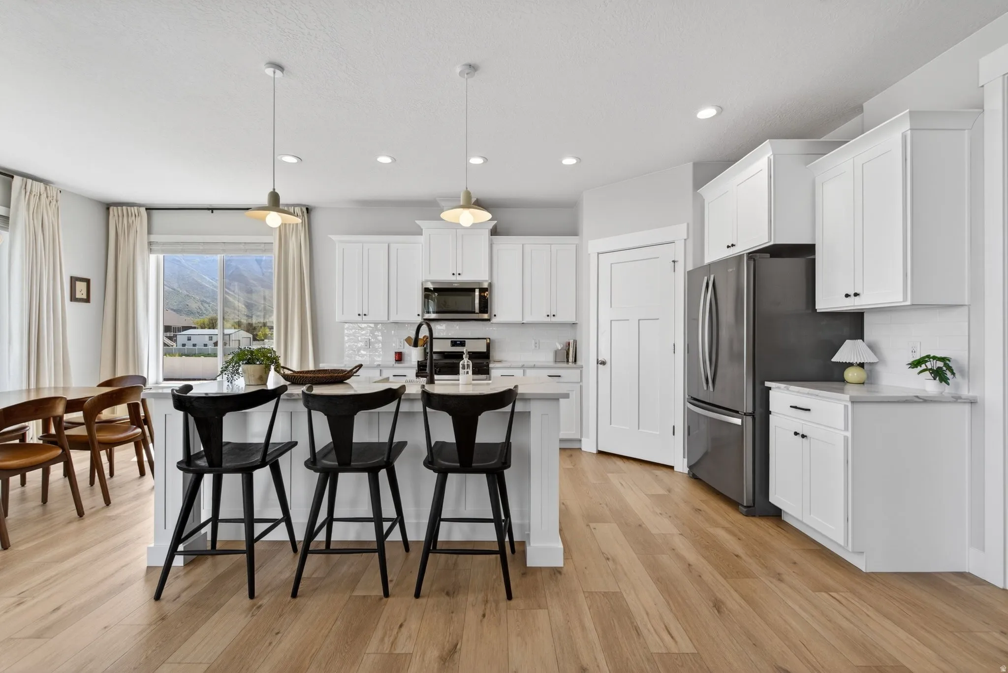 Kitchen with white cabinetry, a breakfast bar, stainless steel appliances, a center island with sink, and hanging light fixtures