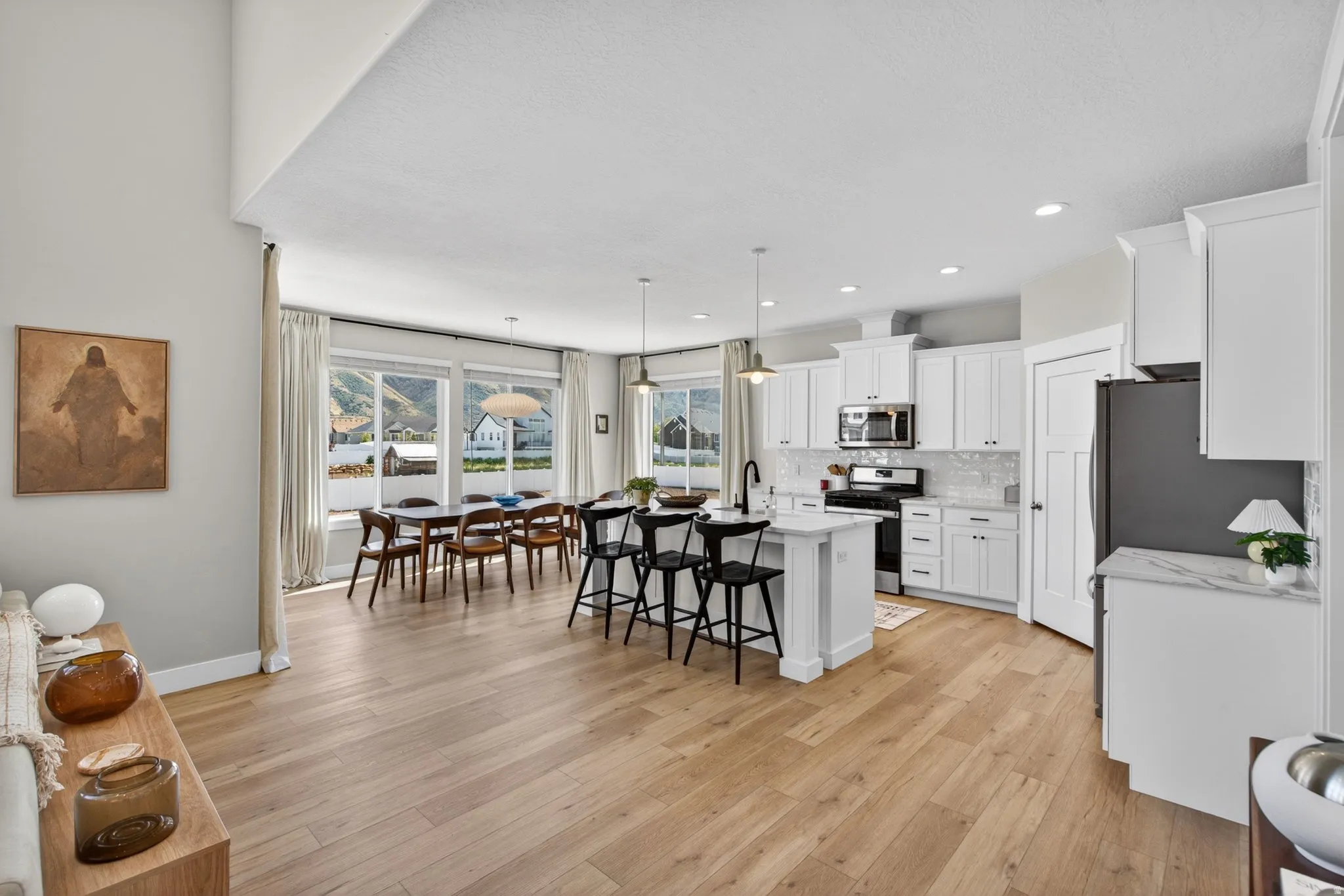 Kitchen featuring stainless steel appliances, a breakfast bar, white cabinetry, an island with sink, and decorative light fixtures