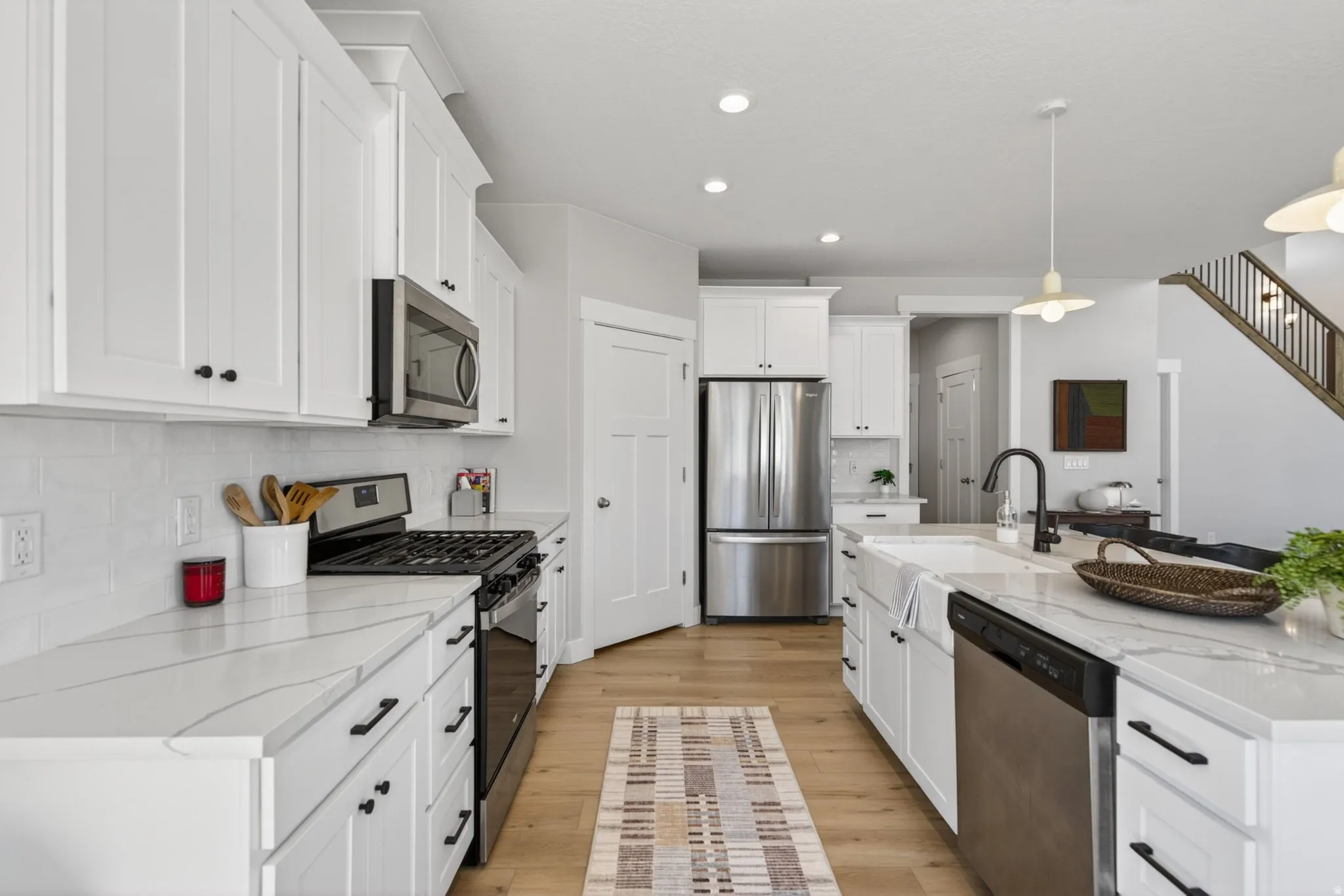 Kitchen featuring stainless steel appliances, white cabinets, light stone counters, backsplash, and a center island with sink