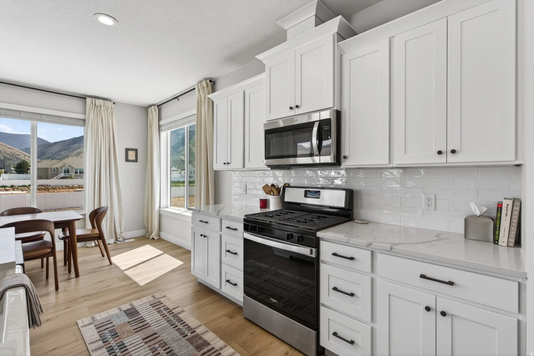 Kitchen with stainless steel appliances, white cabinets, light stone counters, and recessed lighting