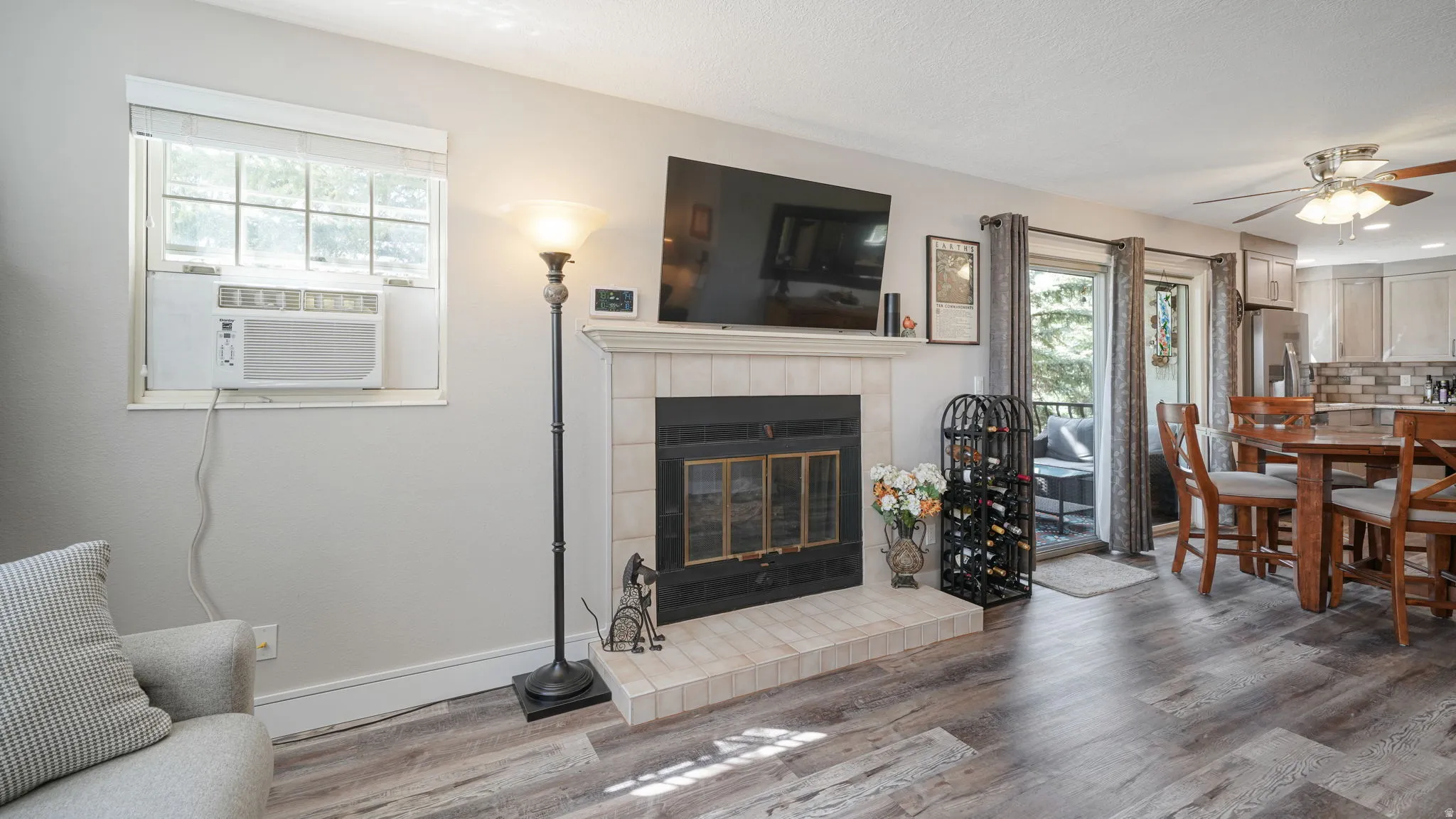 Living room with ceiling fan, a tiled fireplace, wood finished floors, and cooling unit
