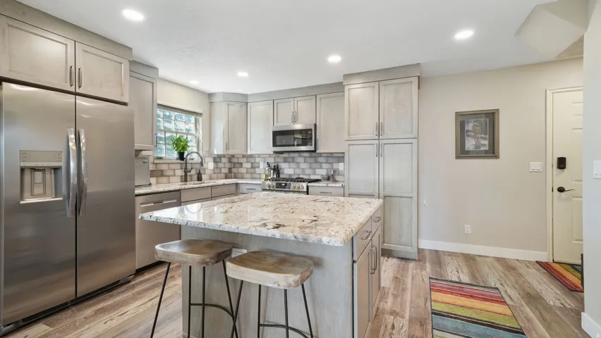 Kitchen featuring stainless steel appliances, light stone countertops, a kitchen island, a breakfast bar, and light wood finished floors