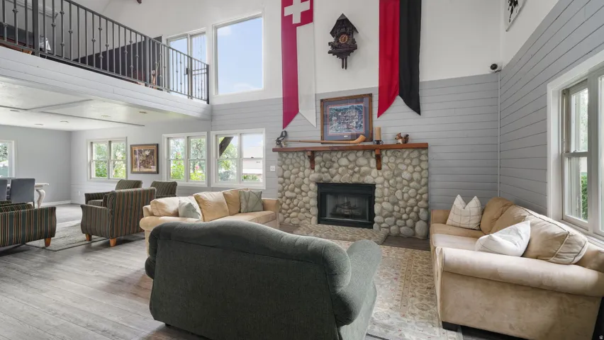 Living area with hardwood / wood-style floors, a stone fireplace, wooden walls, healthy amount of natural light, and a high ceiling