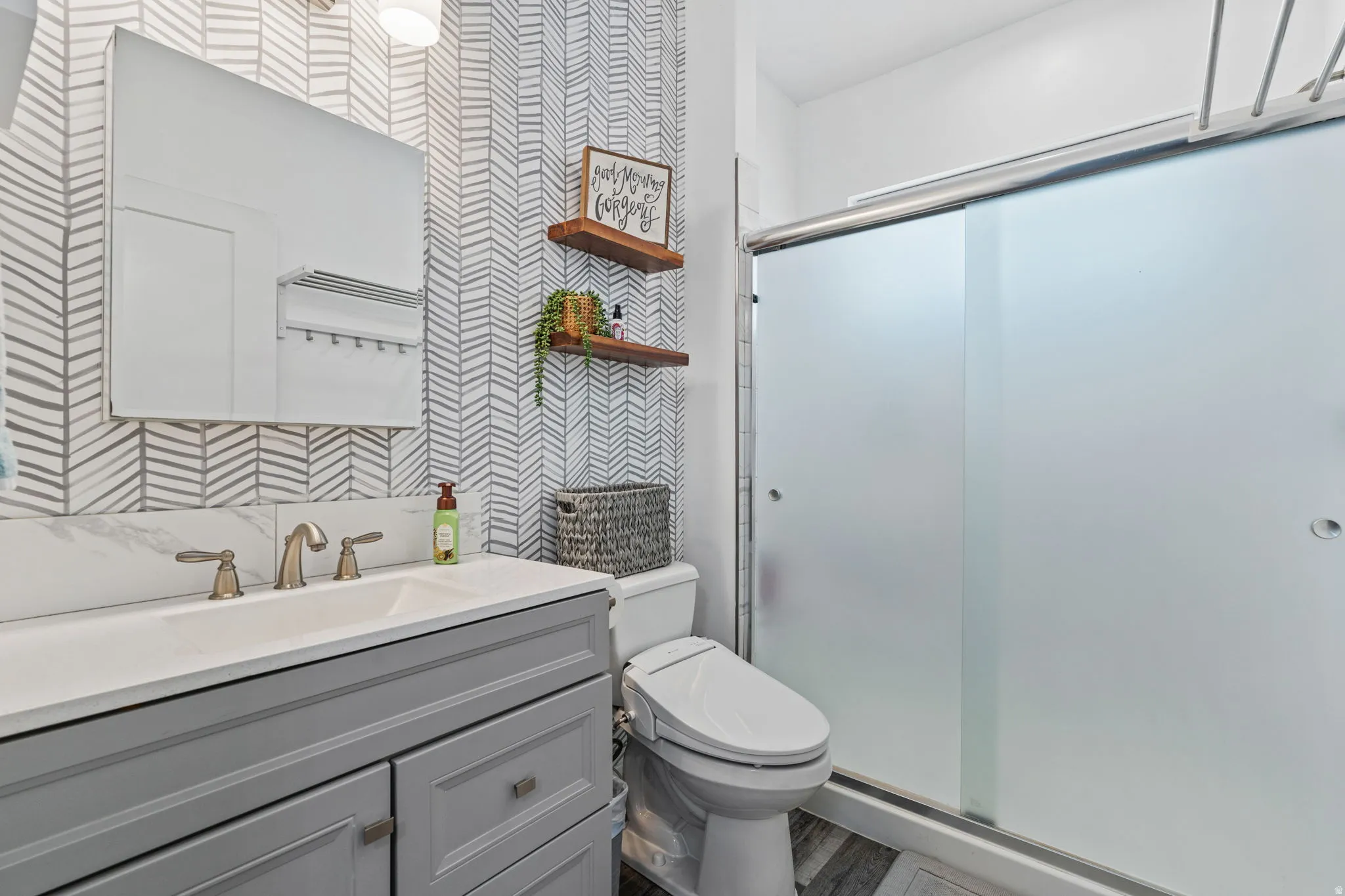 Full bathroom featuring wallpapered walls, vanity, and a shower stall