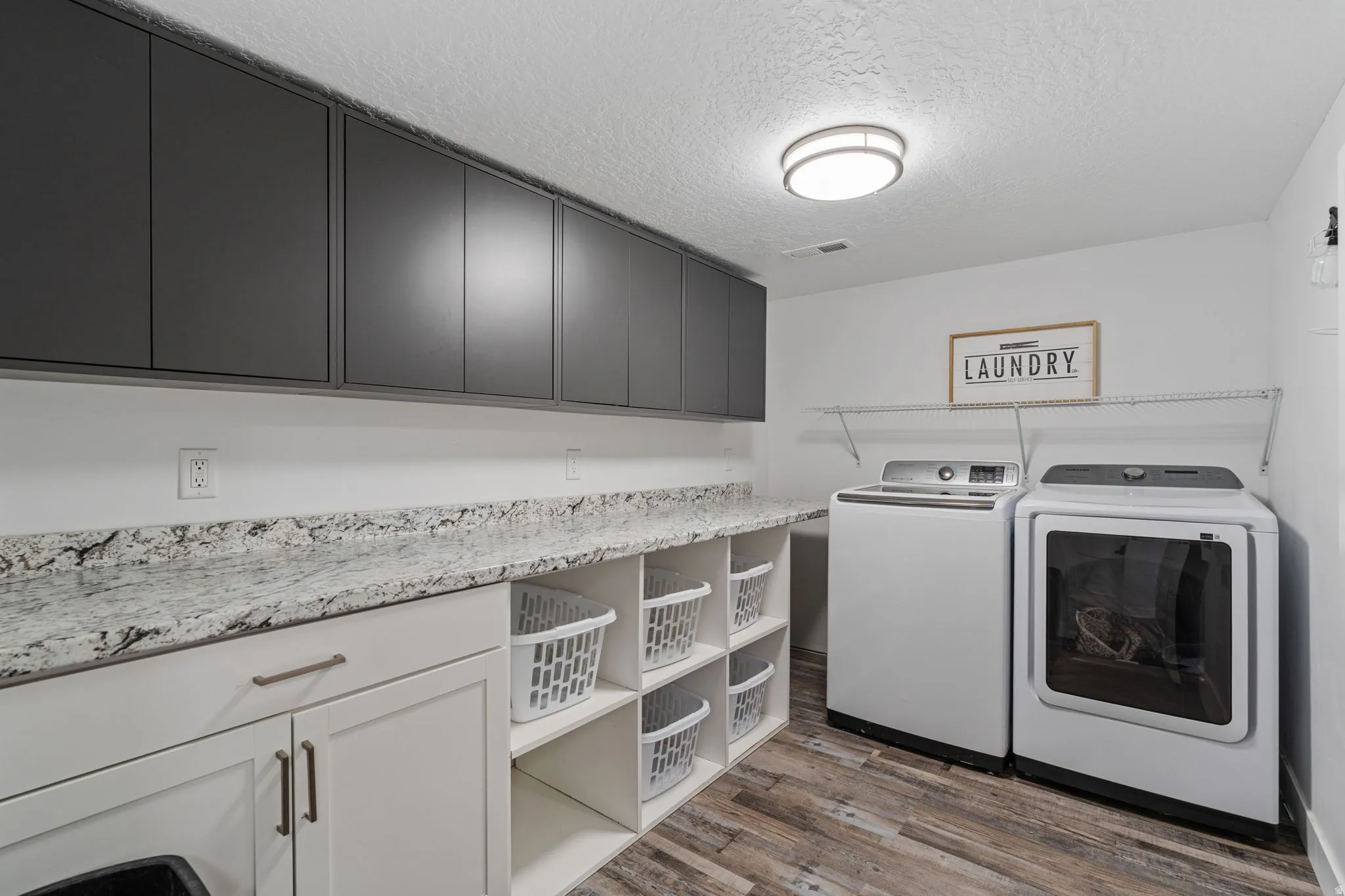 Laundry area with a textured ceiling, light wood-style floors, independent washer and dryer, and cabinet space