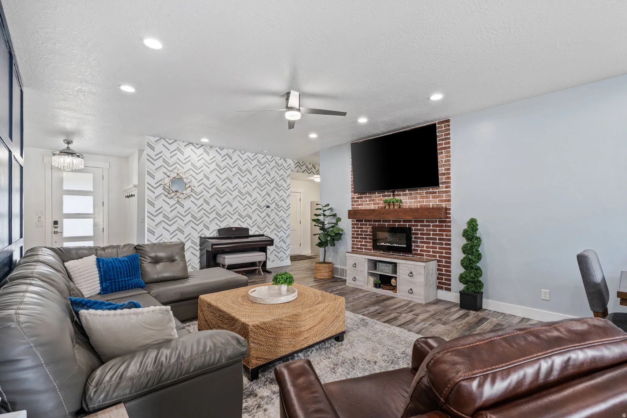 Living room with a ceiling fan, an accent wall, wood finished floors, recessed lighting, and a brick fireplace