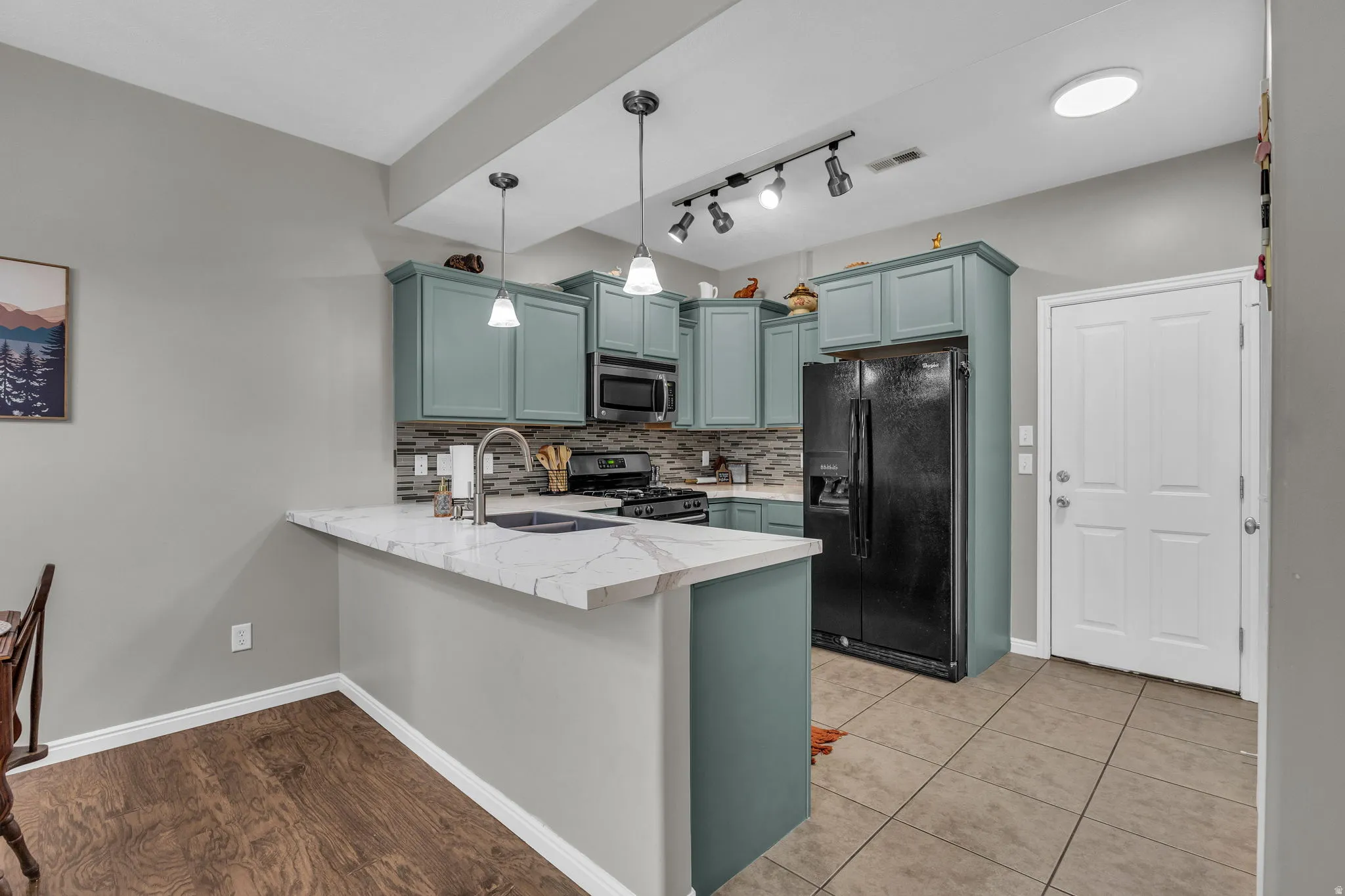 Kitchen with backsplash, stainless steel appliances, a peninsula, a kitchen breakfast bar, and light stone countertops