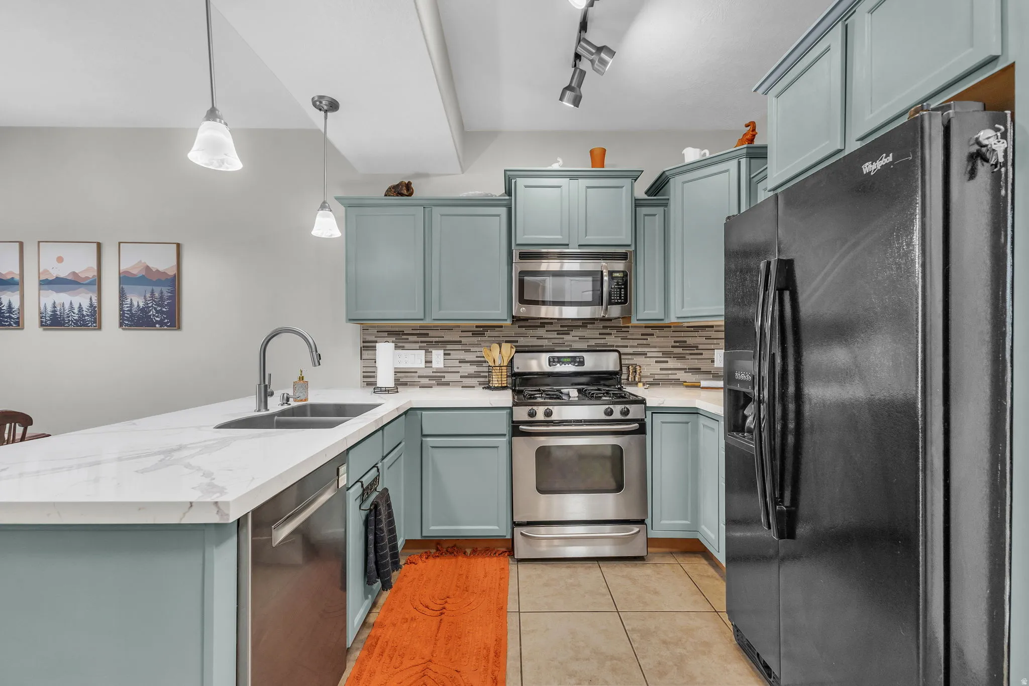Kitchen with stainless steel appliances, a peninsula, tasteful backsplash, light tile patterned floors, and light stone countertops