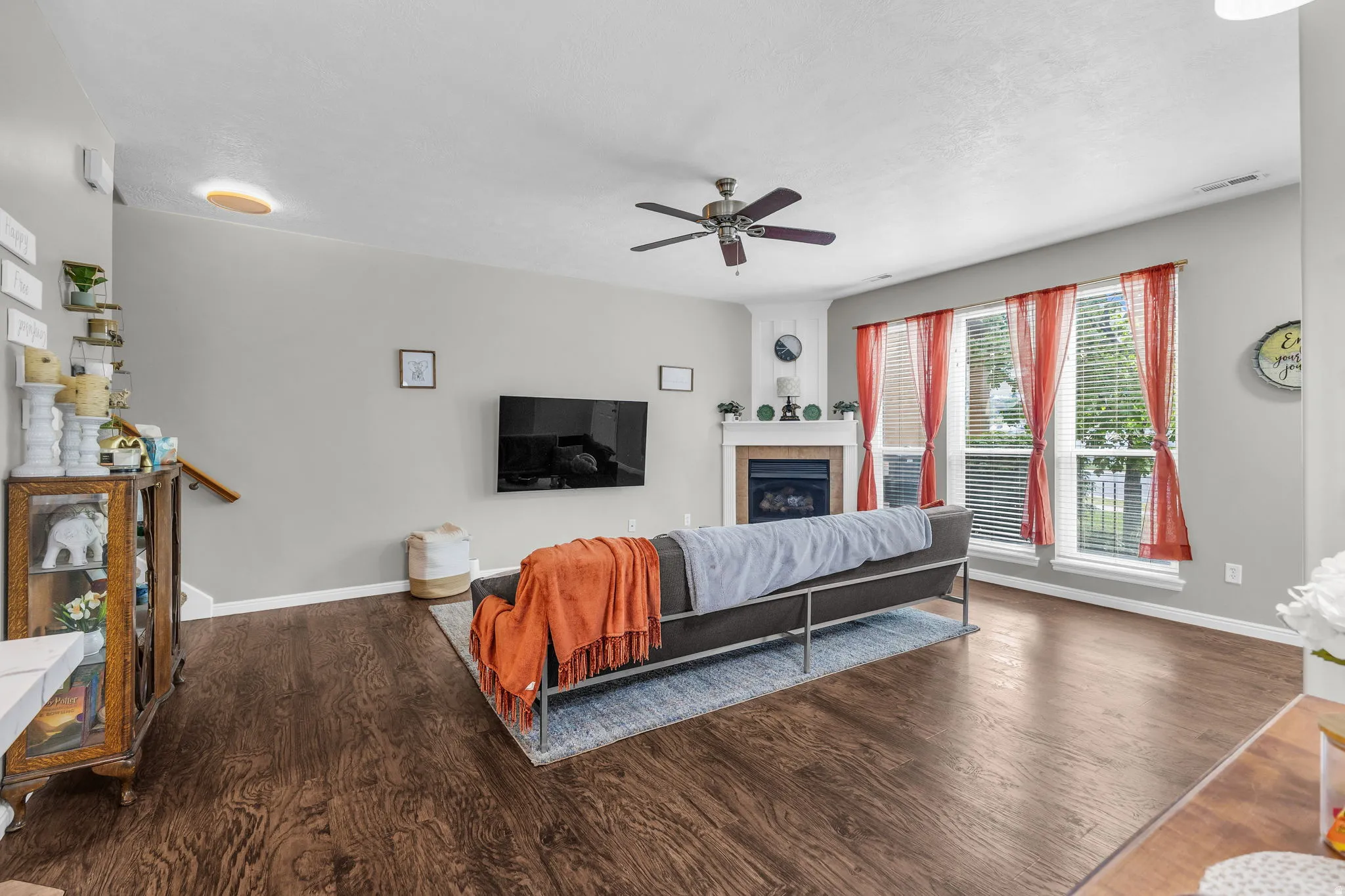 Living area with ceiling fan, a tile fireplace, and wood finished floors