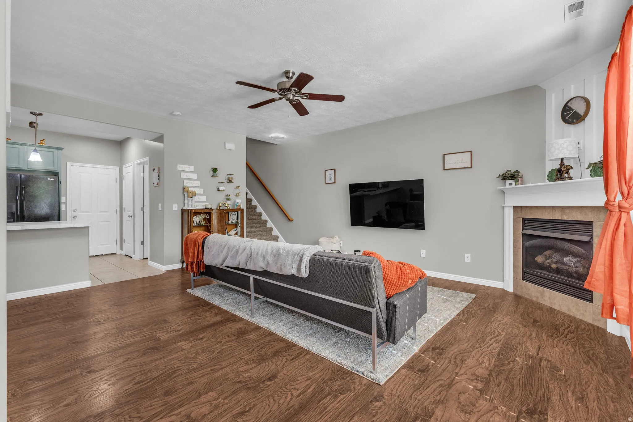 Living room with ceiling fan, light wood finished floors, a tiled fireplace, and a textured ceiling