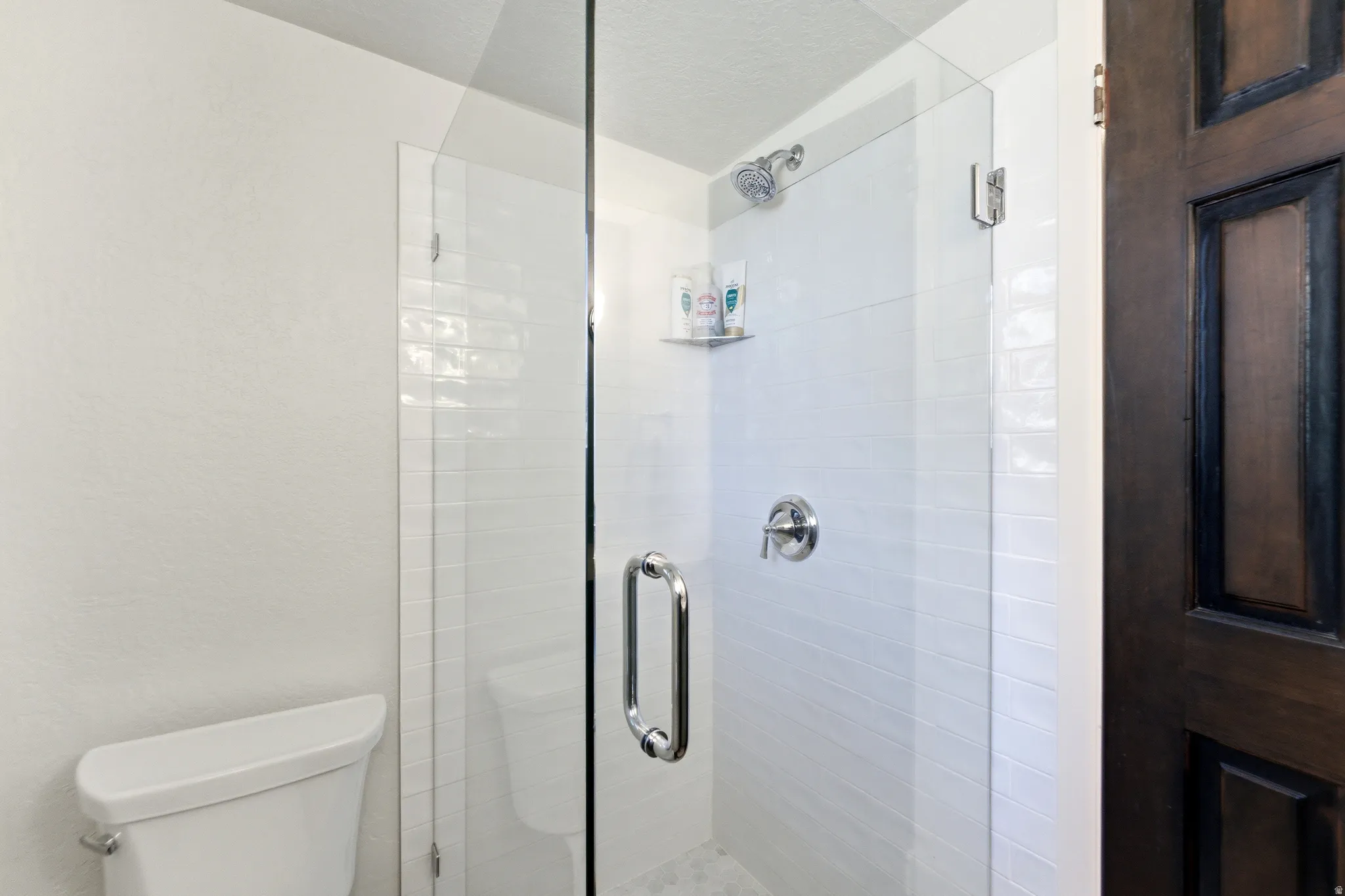 Bathroom with a stall shower, a textured ceiling, and a textured wall