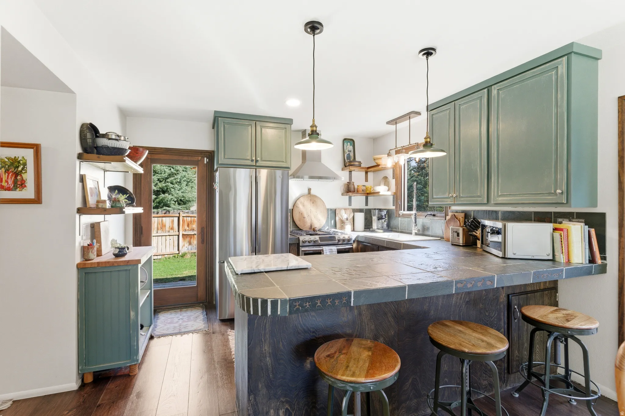 Kitchen with green cabinets, a peninsula, dark wood finished floors, stainless steel appliances, and open shelves