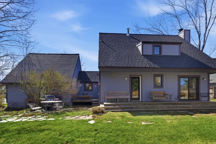 Rear view of house featuring a lawn, a porch, roof with shingles, and a chimney