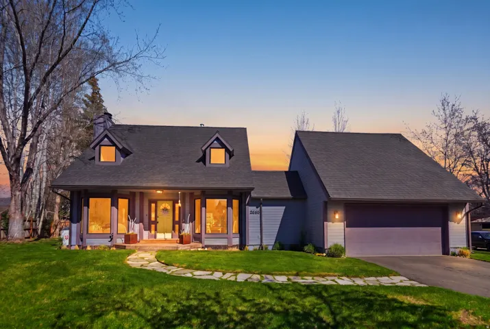 View of front of property with covered porch, a front yard, asphalt driveway, a chimney, and an attached garage