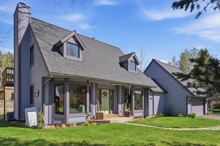 Cape cod-style house featuring a front yard, a porch, a chimney, roof with shingles, and a garage