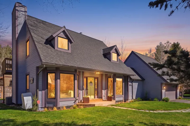 View of front of house featuring covered porch, a front yard, a chimney, roof with shingles, and a garage