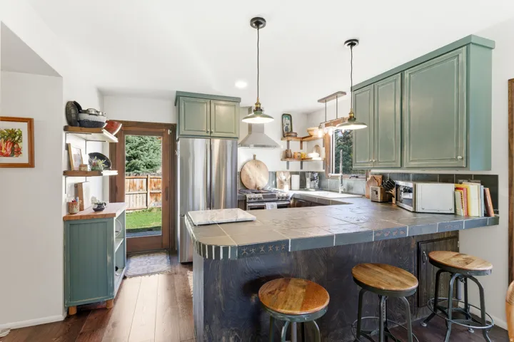 Kitchen with green cabinets, a peninsula, dark wood finished floors, stainless steel appliances, and open shelves