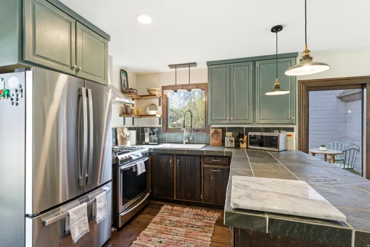 Kitchen with stainless steel appliances, pendant lighting, green cabinets, dark wood finished floors, and a peninsula