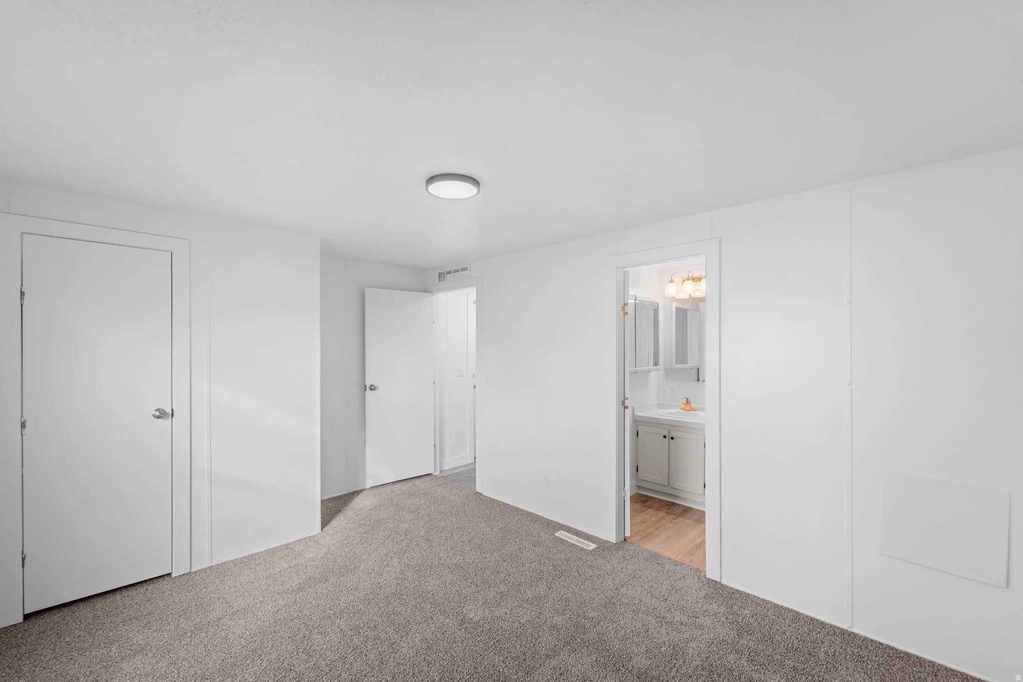 Unfurnished bedroom featuring light colored carpet and connected bathroom