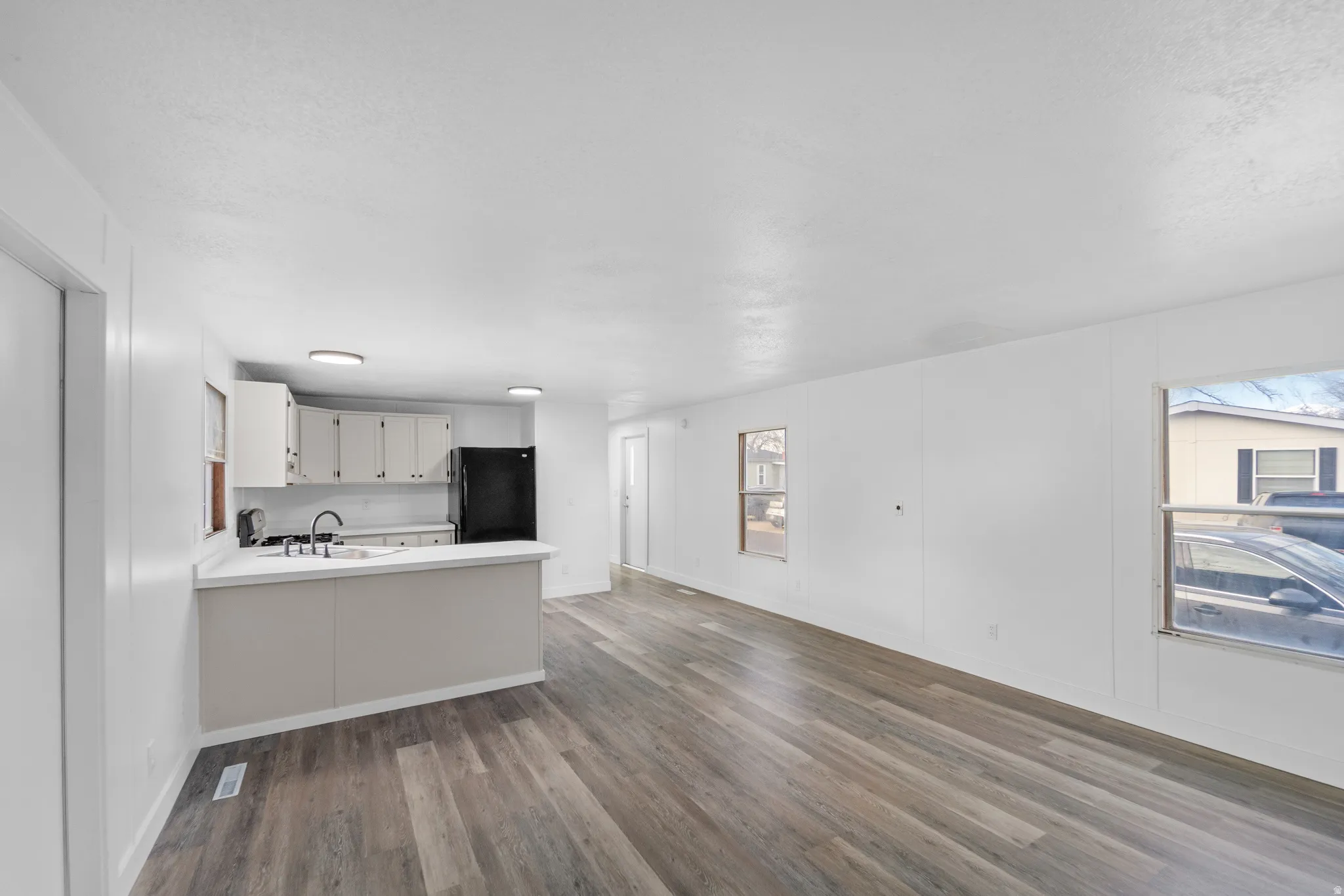 Kitchen with light countertops, dark wood finished floors, freestanding refrigerator, white cabinets, and a peninsula
