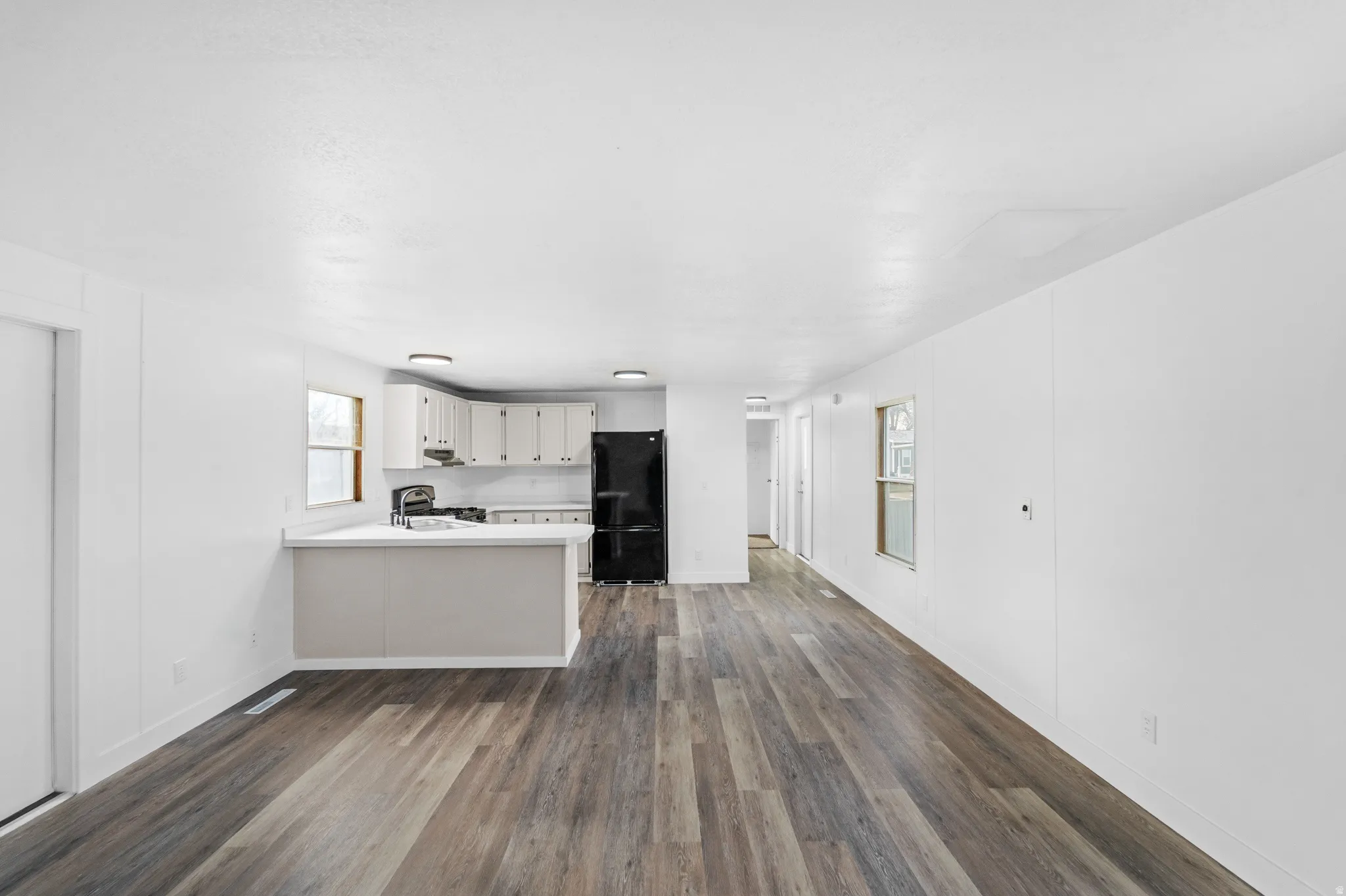 Kitchen featuring light countertops, a peninsula, freestanding refrigerator, dark wood-style floors, and white cabinets