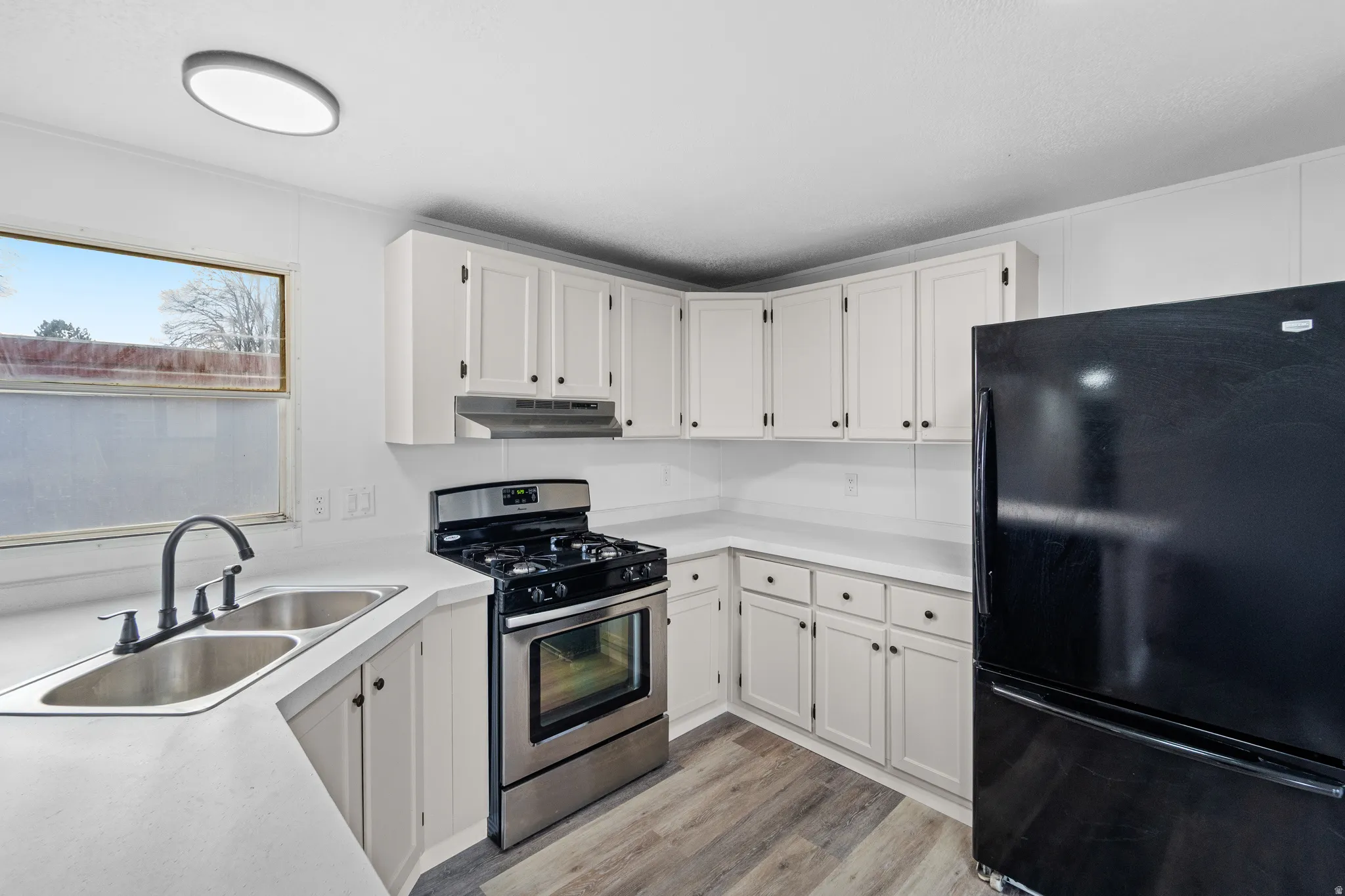 Kitchen with freestanding refrigerator, gas range, light countertops, white cabinetry, and light wood-style floors