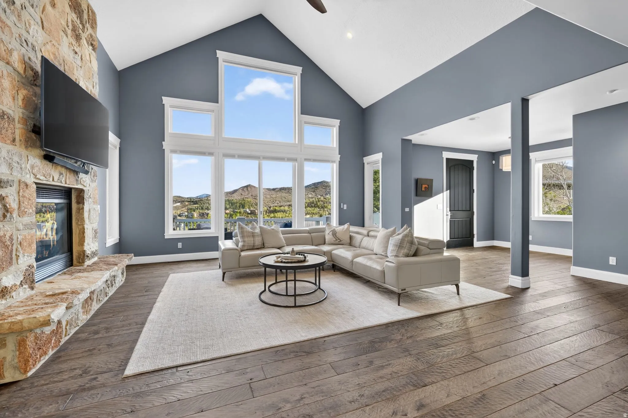 Living room with a stone fireplace, ceiling fan, dark wood finished floors, and a high ceiling