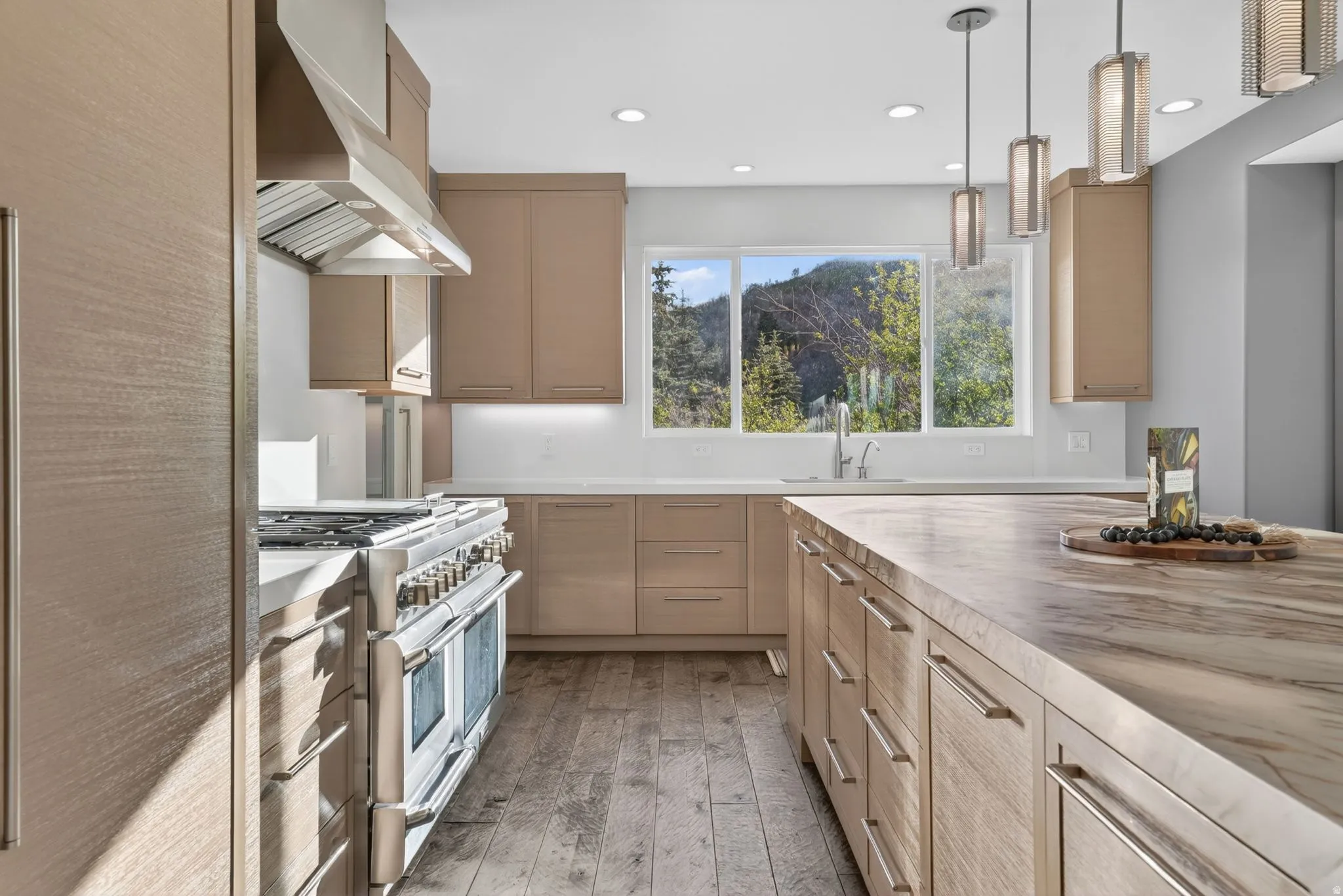Kitchen featuring double oven range, light wood finish cabinets, light wood-type flooring, and hanging light fixtures
